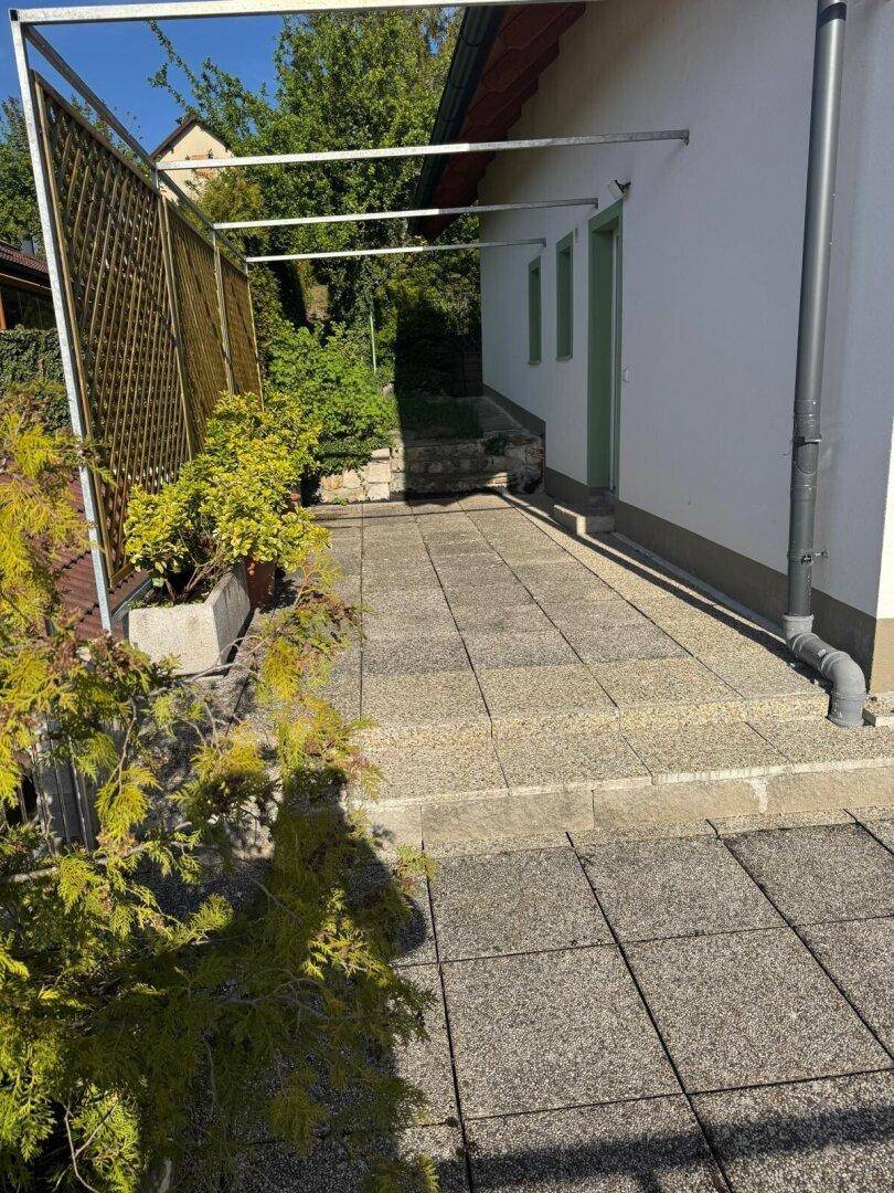 Gepflasterte Terrasse am Haus mit einer Metallkonstruktion, die auf eine zukünftige Überdachung hindeutet.