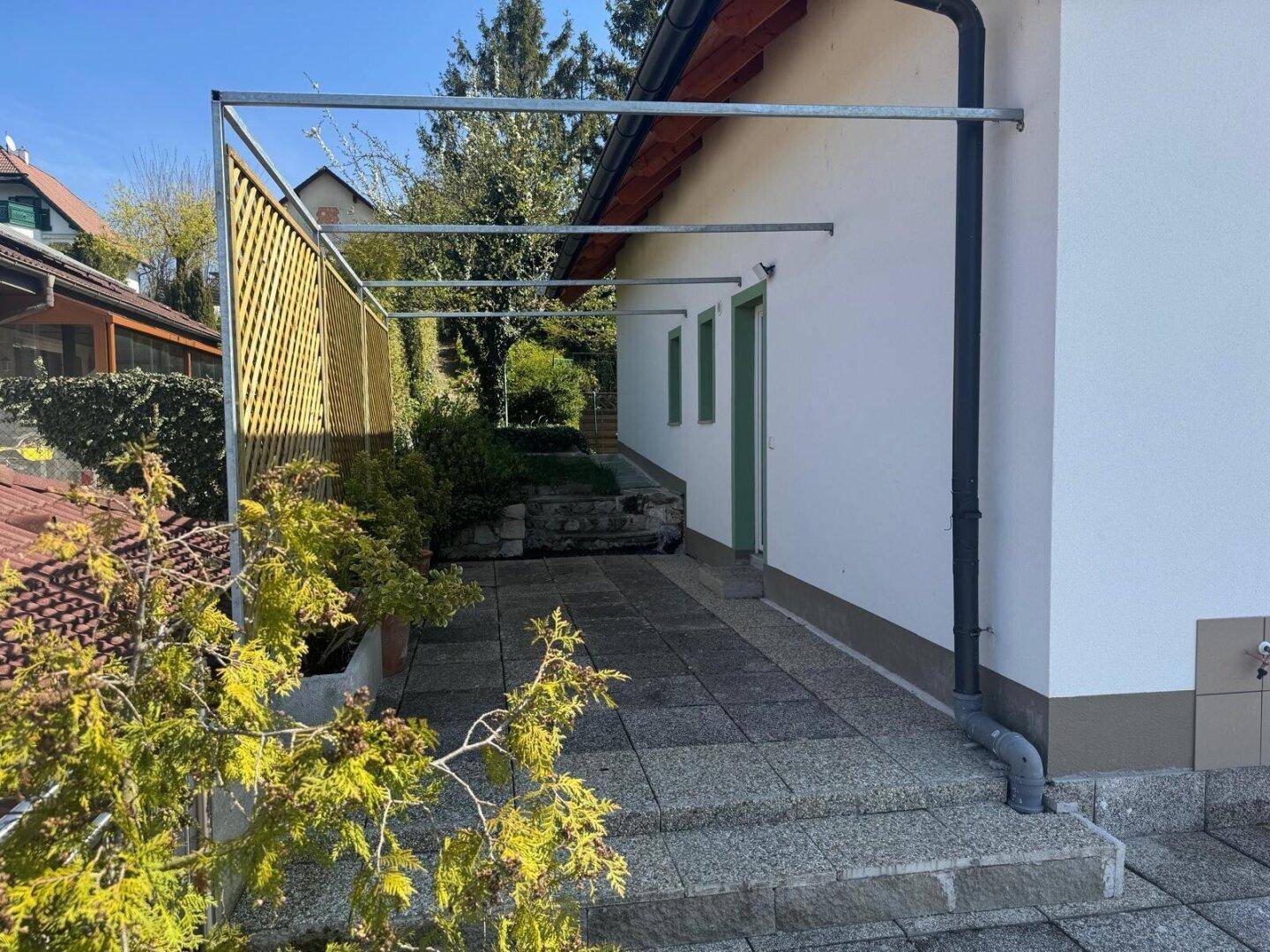 Seitlicher Außenbereich mit gepflastertem Weg und einer Metallkonstruktion für eine zukünftige Überdachung.