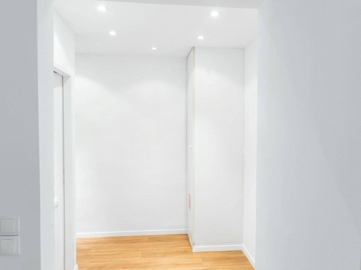 Heller Flur mit Holzboden, weißen Wänden und integrierten Deckenleuchten.