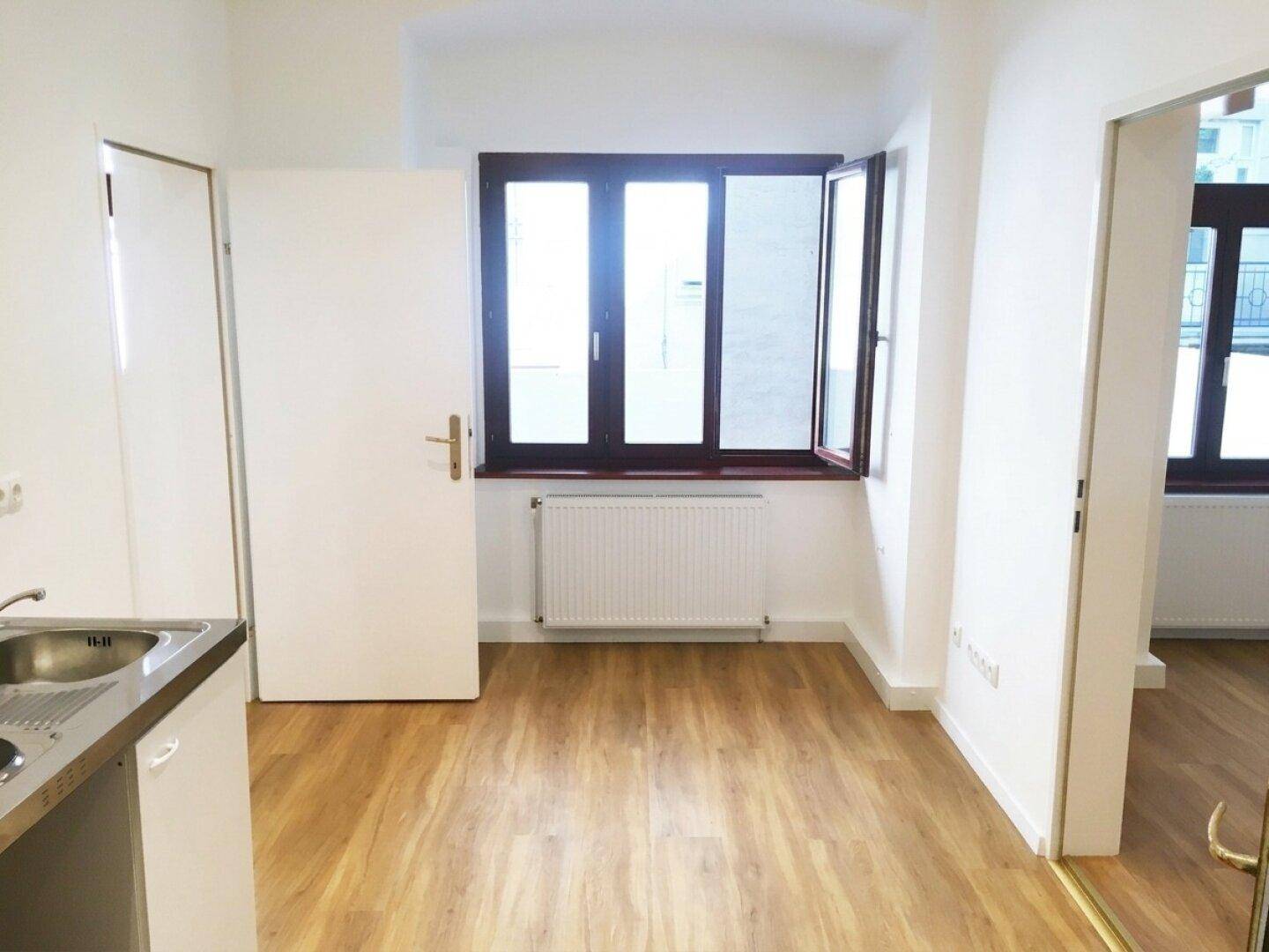 Offener Raum mit Küchenzeile, Holzboden und einem geöffneten Fenster.