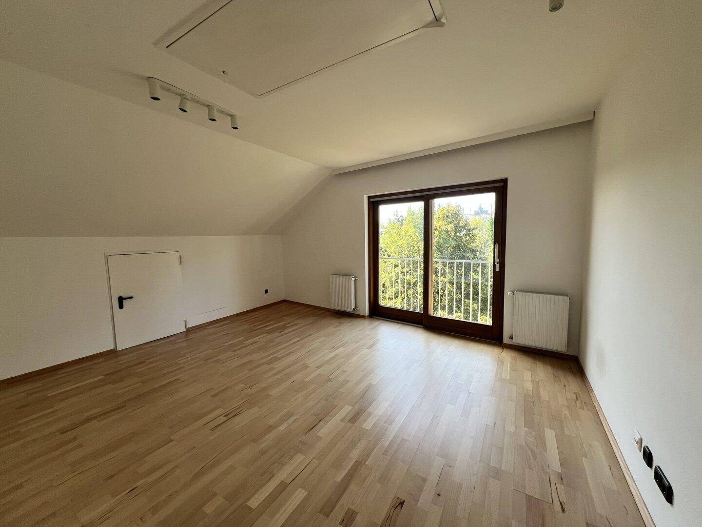 Helles Dachzimmer mit Holzboden, Zugang zu einem französischen Balkon und Blick ins Grüne.