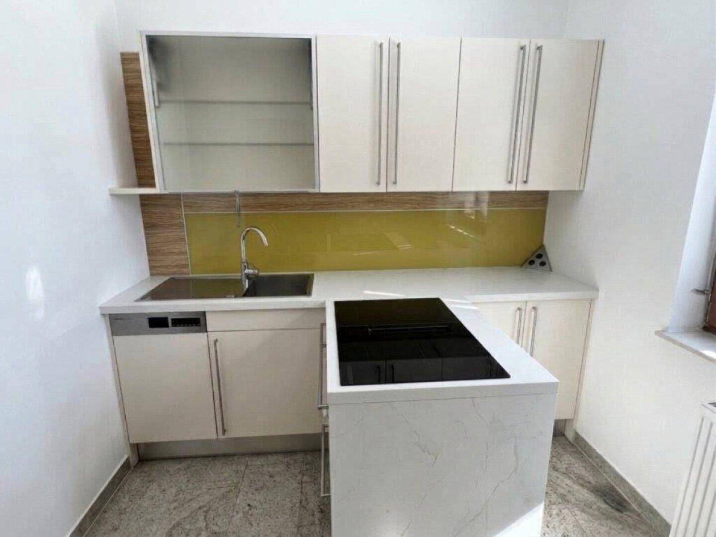 Moderne Küchenzeile mit weißen Schränken, Induktionskochfeld und gelber Rückwand.