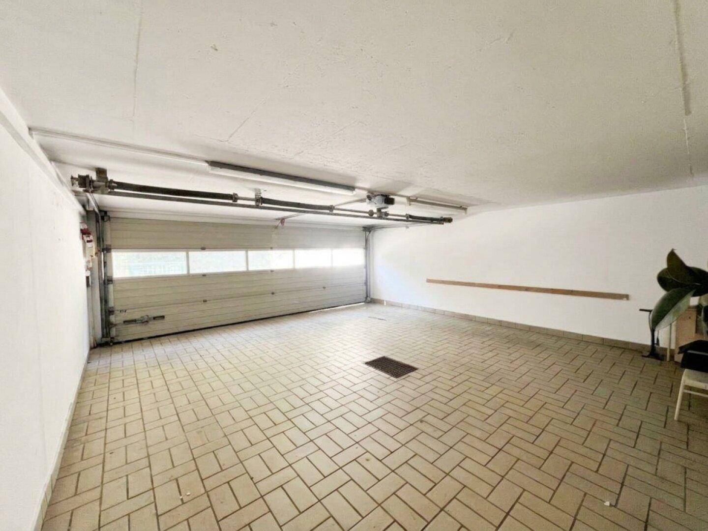 Geräumige leere Garage mit Fliesenboden und einem breiten Garagentor.