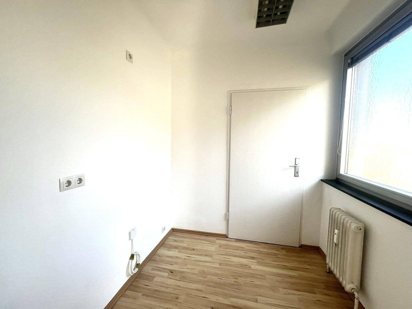 Kleines helles Zimmer mit Laminatboden, Fenster und Heizkörper.