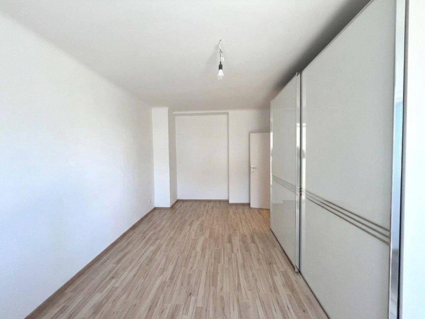 Geräumiges Zimmer mit hellem Laminatboden und großem weißen Schiebetürenschrank.