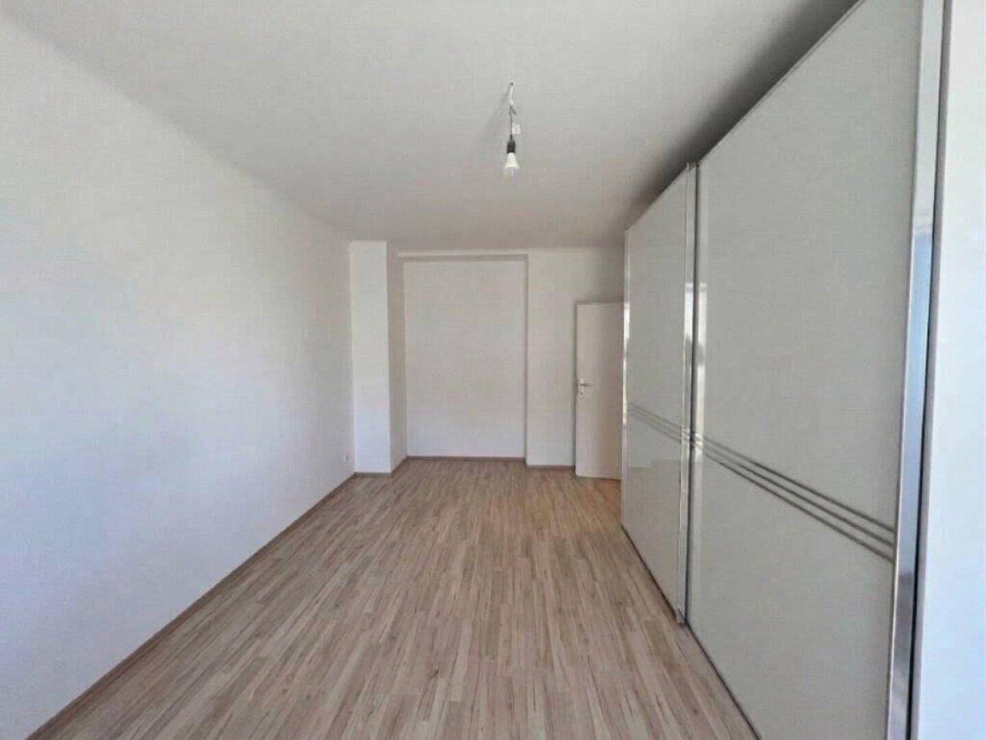 Geräumiges Zimmer mit hellem Laminatboden und großem weißen Schiebetürenschrank.