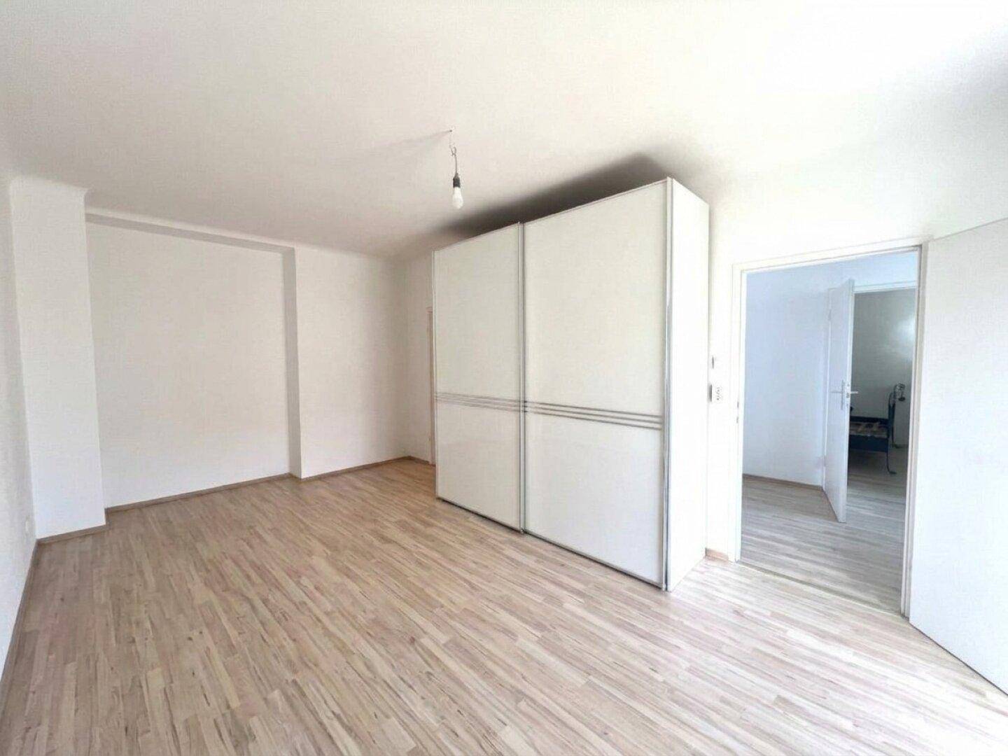 Helles Schlafzimmer mit Laminatboden, weißem Kleiderschrank und Zugang zu einem weiteren Raum.