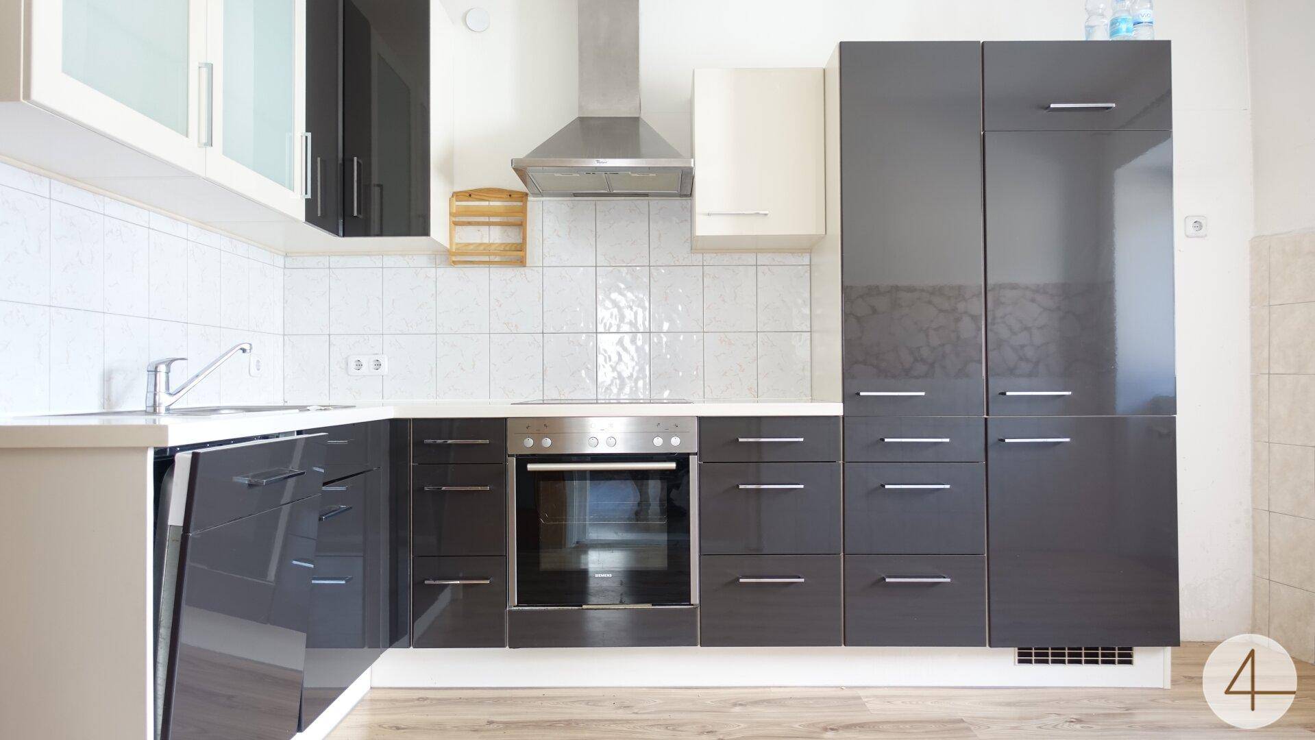 Moderne Küche mit grauen Hochglanzfronten, weißen Arbeitsplatten und integrierten Geräten.
