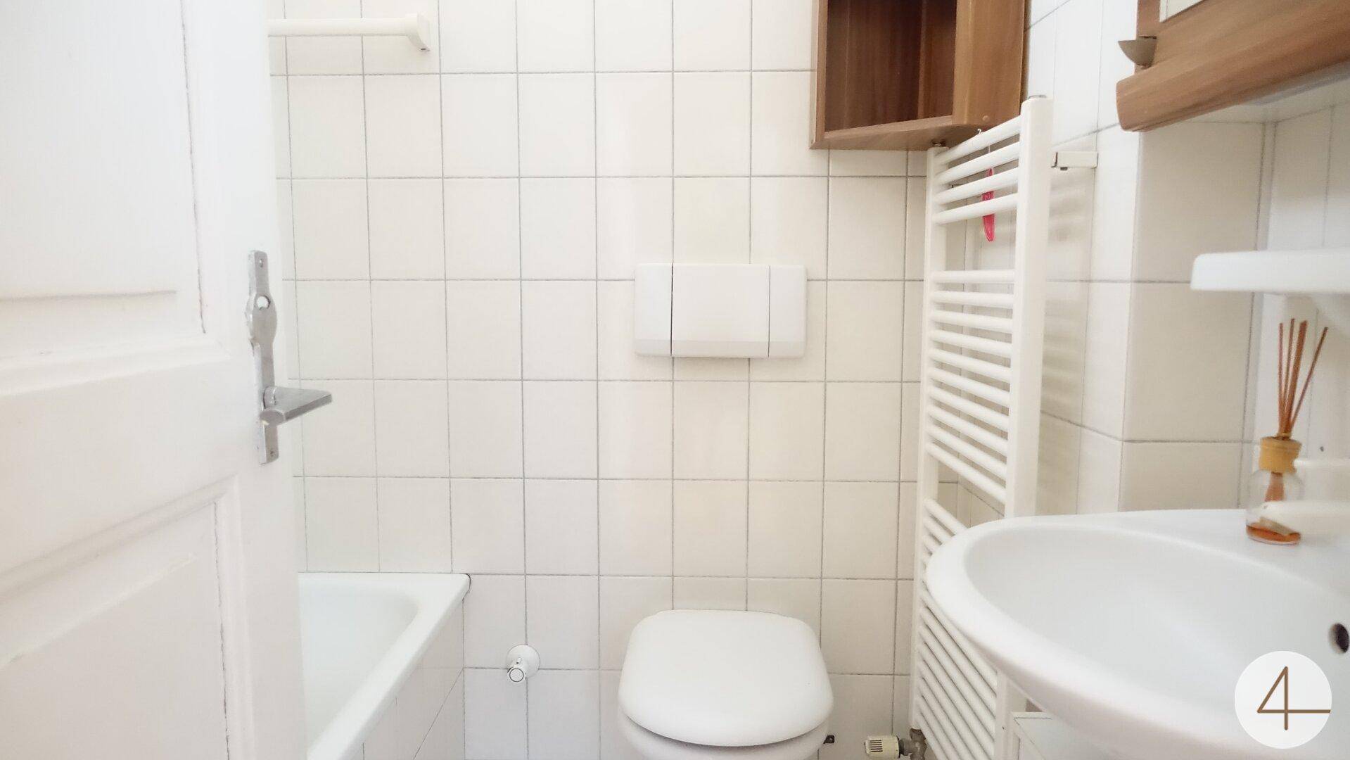 Helles Badezimmer mit weißen Fliesen, Badewanne, WC und beheiztem Handtuchhalter.