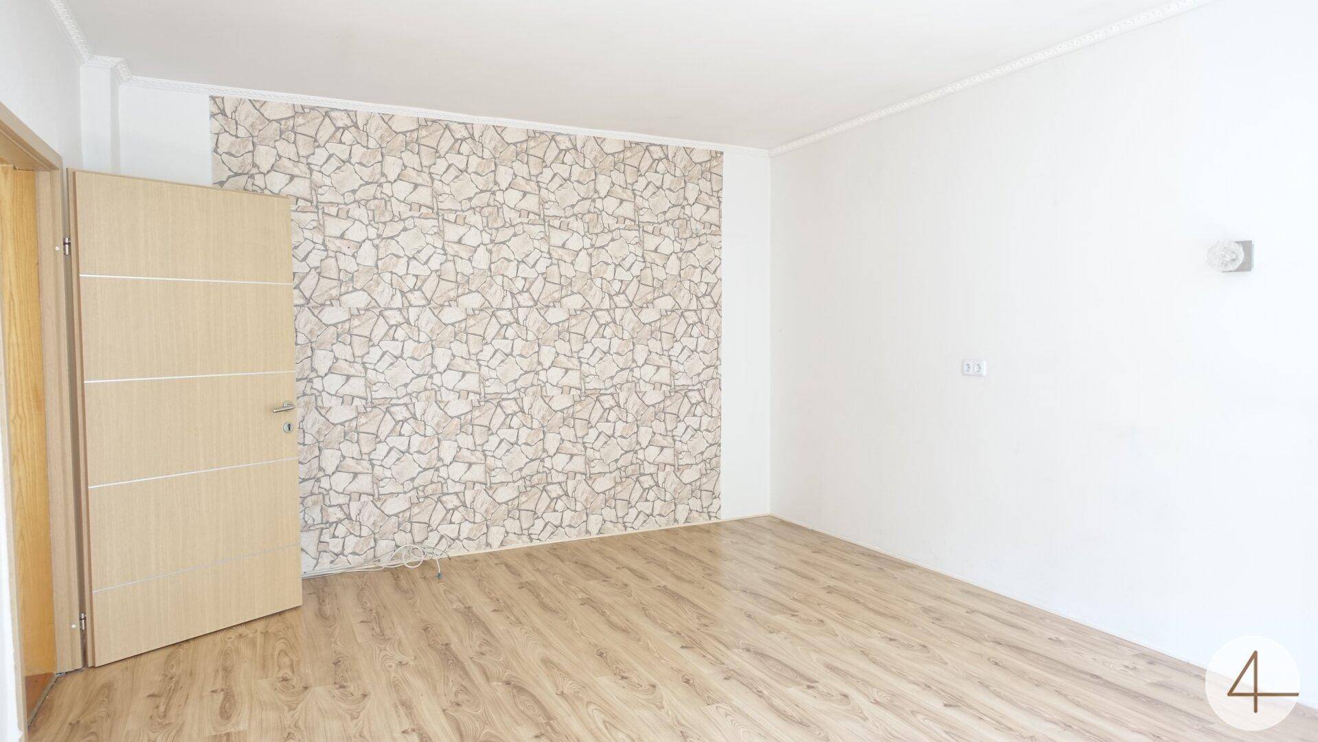 Leerer Raum mit Laminatboden und einer Akzentwand in Steinoptik.