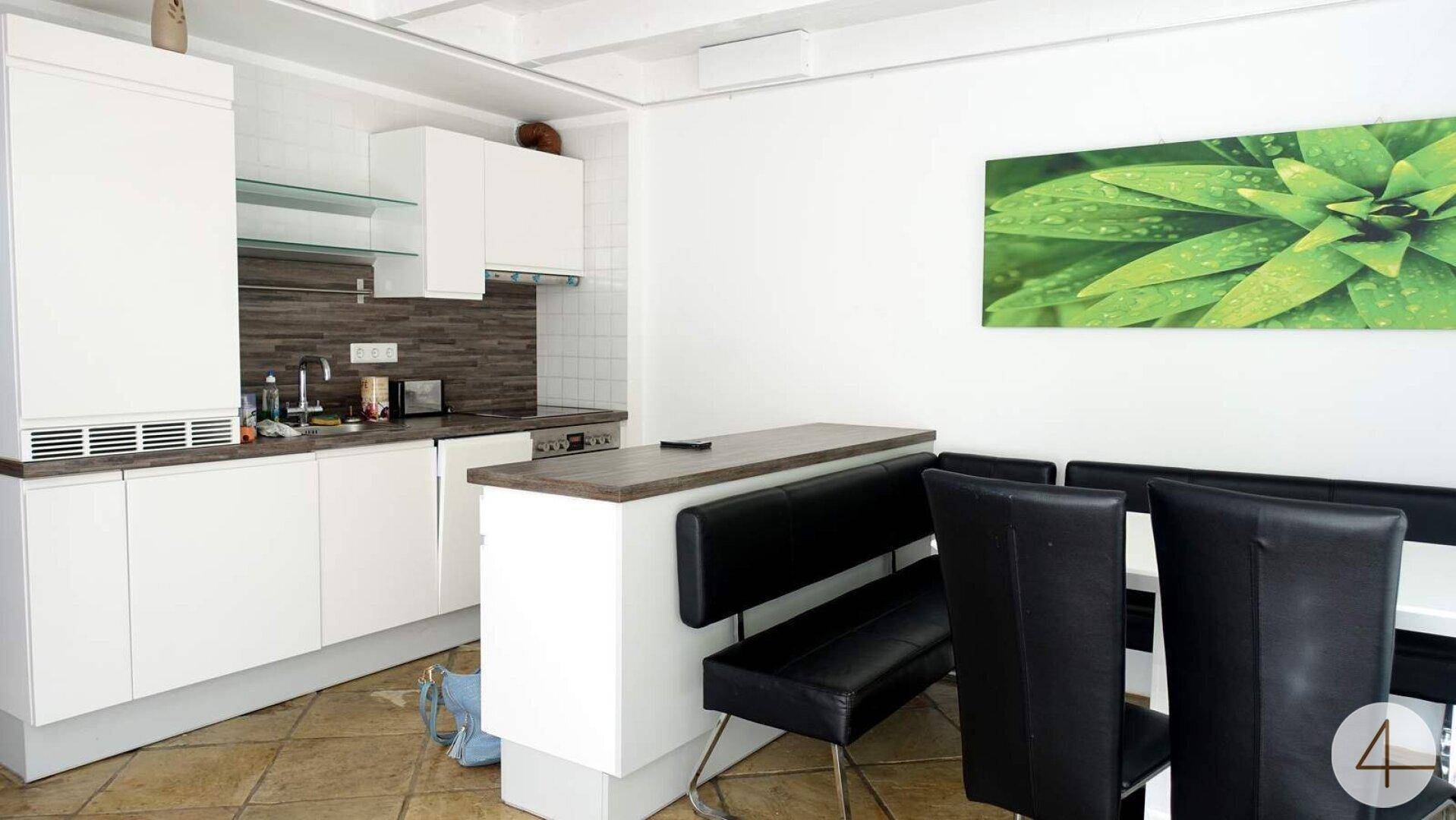 Moderne weiße Küche mit integrierten Geräten, Essbereich und Fliesenboden.