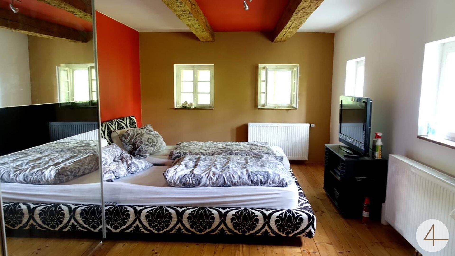 Gemütliches Schlafzimmer mit Holzbalken, farbigen Wänden und einem großen Doppelbett.