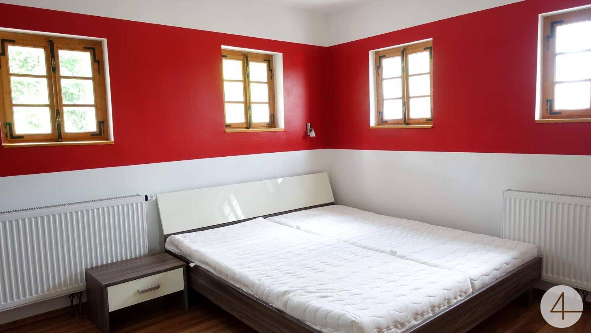 Helles Schlafzimmer mit rot-weißen Wänden, Doppelbett und Holzfenstern.