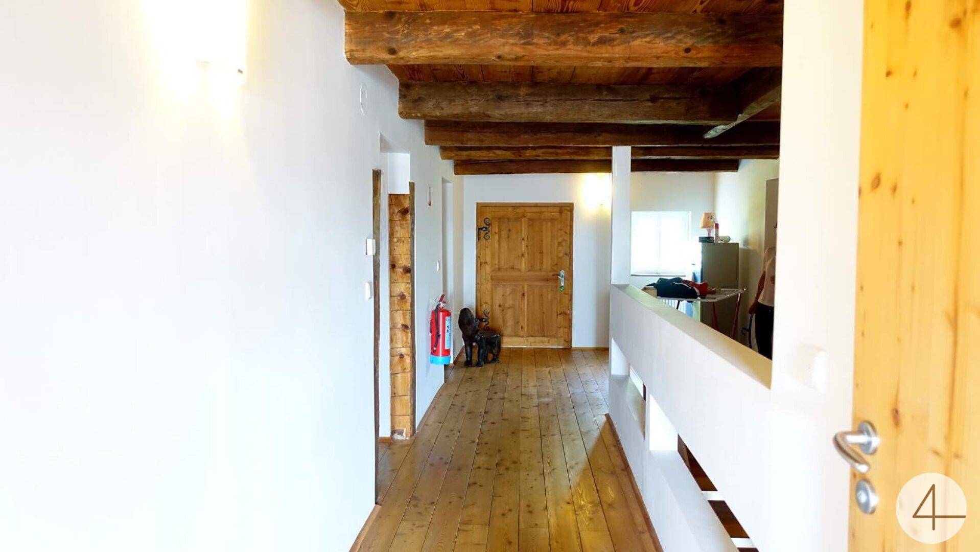 Heller Flur mit Holzdielenboden, sichtbaren Deckenbalken und weiß gestrichenen Wänden.