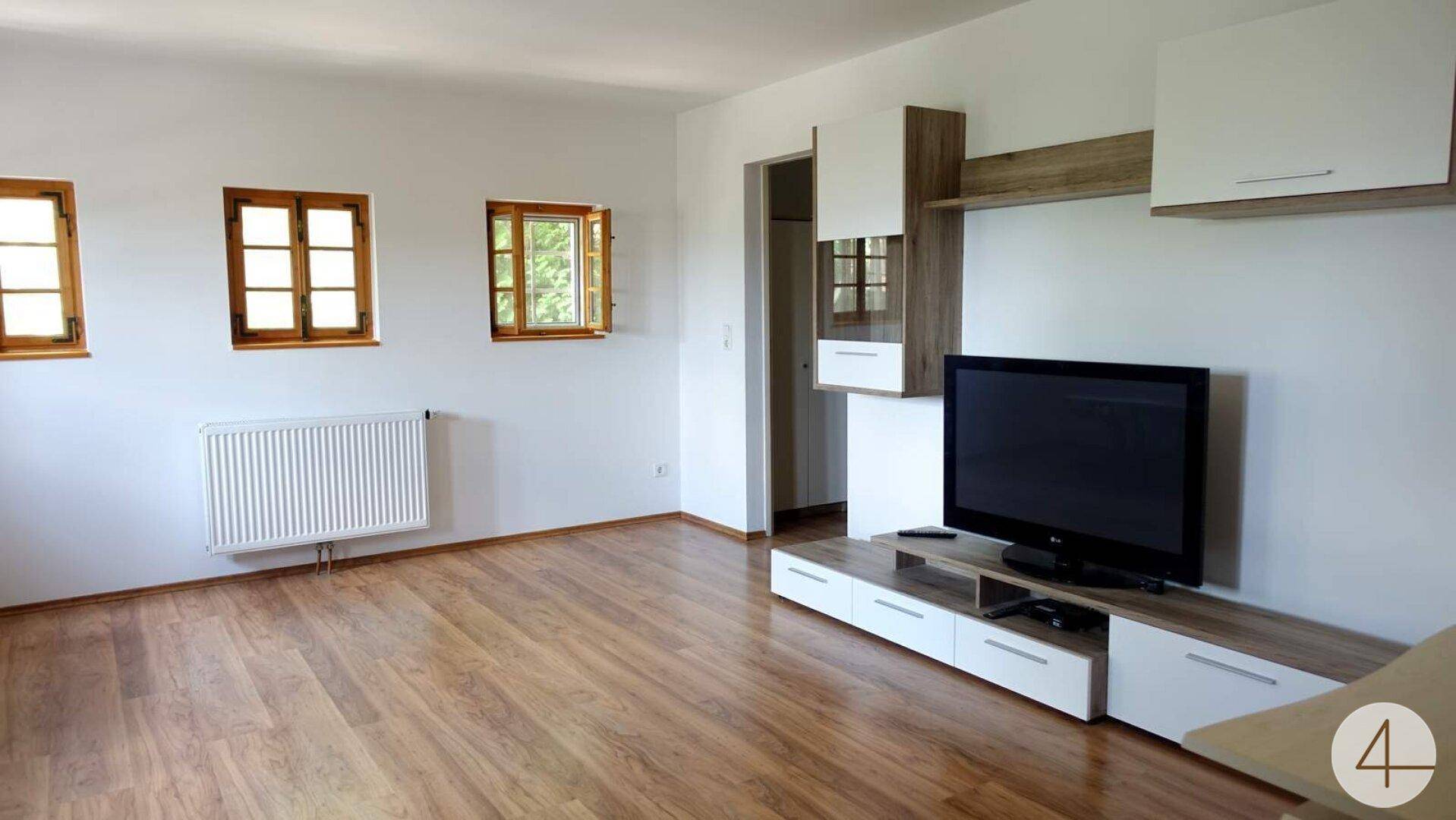 Geräumiges Wohnzimmer mit Holzboden, weißen Wänden und einem modernen TV-Möbel.