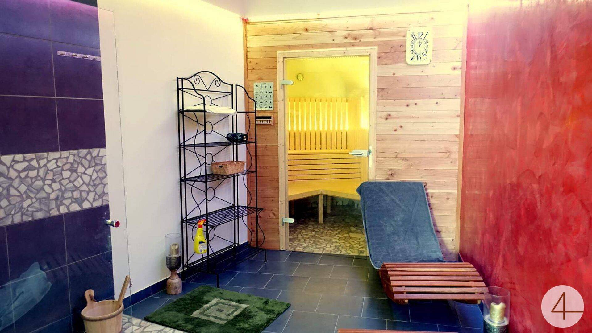 Entspannungsbereich mit Liege und Zugang zu einer Holzsauna, umgeben von Fliesen.