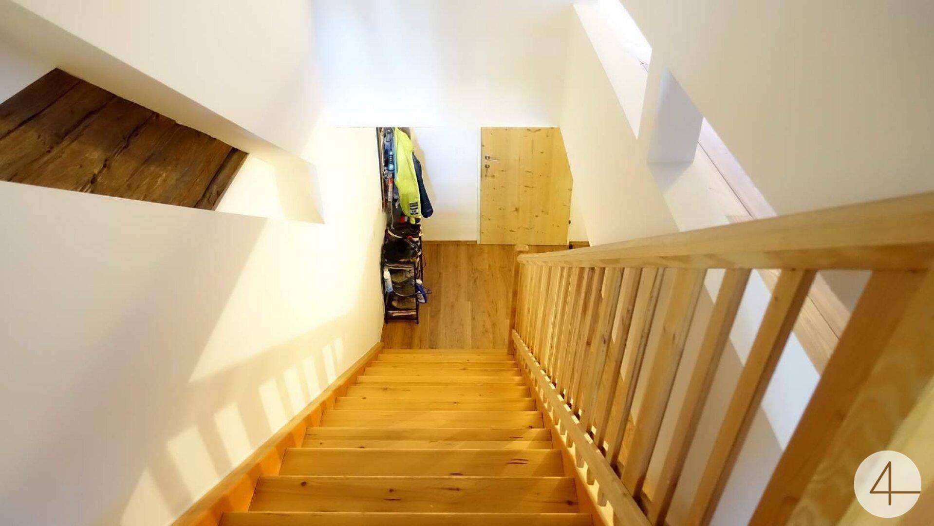 Holztreppe führt in einen unteren Bereich mit Dachschrägen und Stauraum.