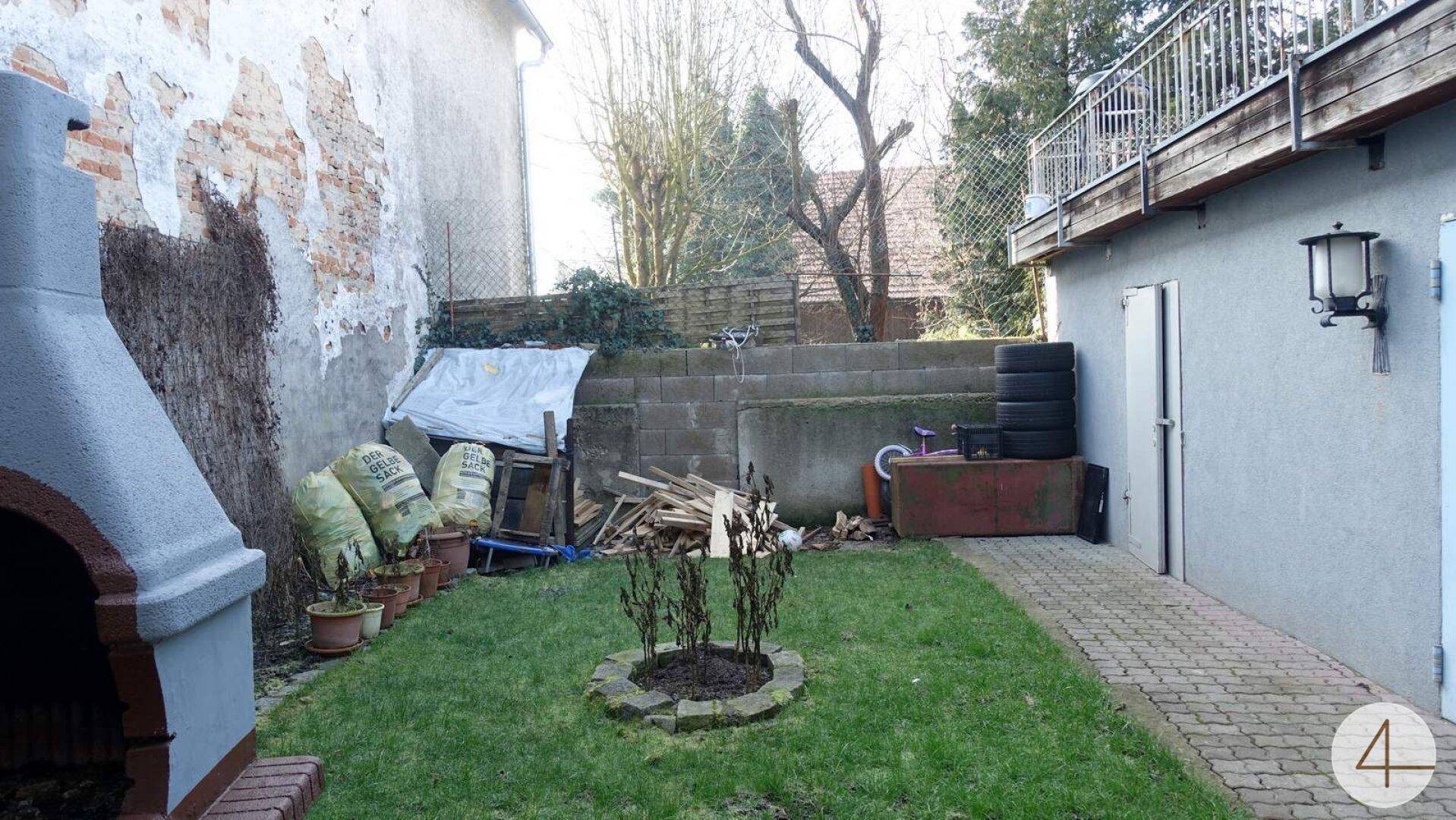Hinterhof mit Rasenfläche, Grillplatz und einer alten Ziegelmauer im Hintergrund.