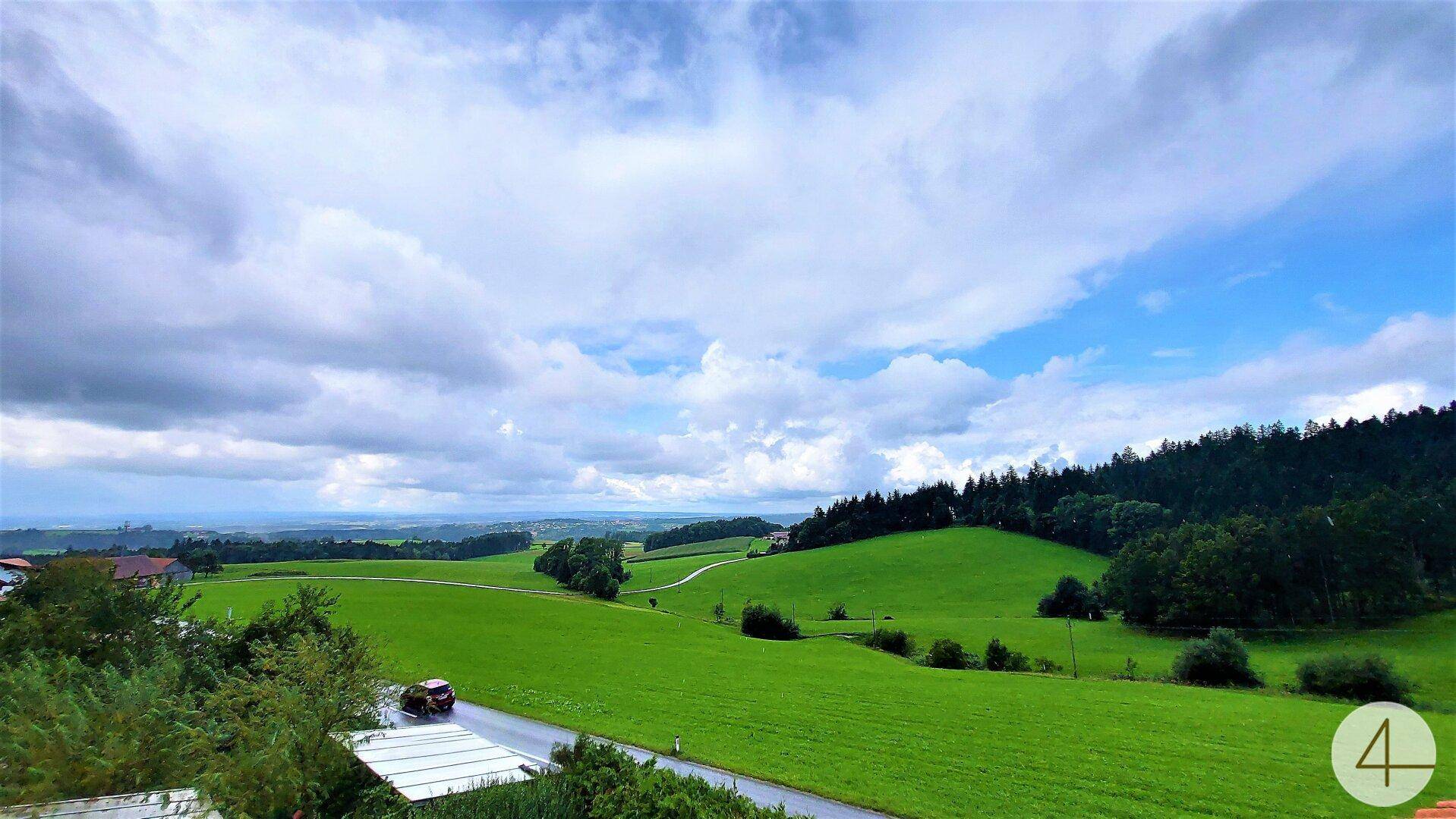 Panoramablick über die weite grüne Landschaft mit Feldern und Wäldern unter bewölktem Himmel.