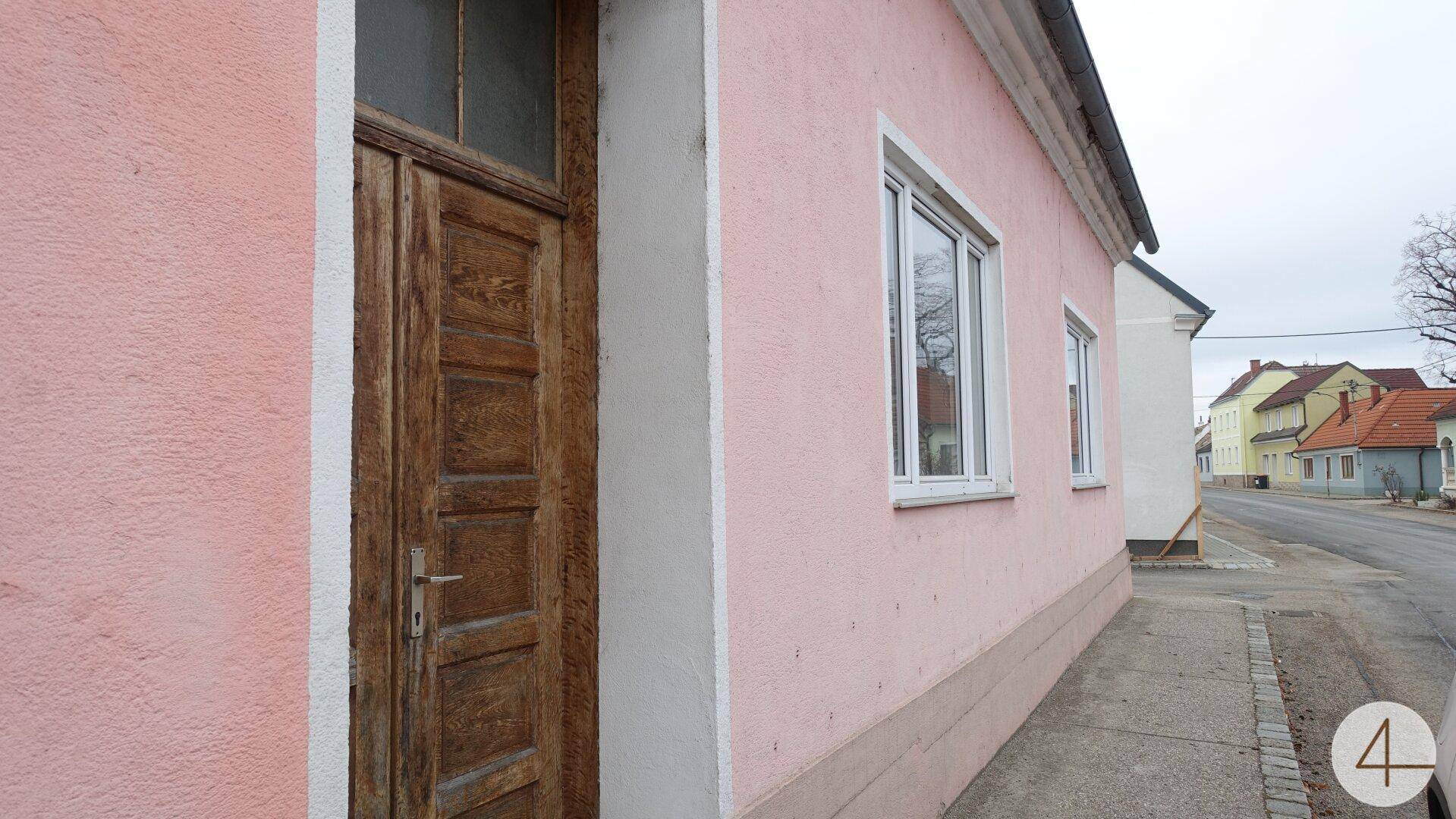 Detailansicht der rosafarbenen Fassade mit einer rustikalen Holztür und einem modernen weißen Fenster.
