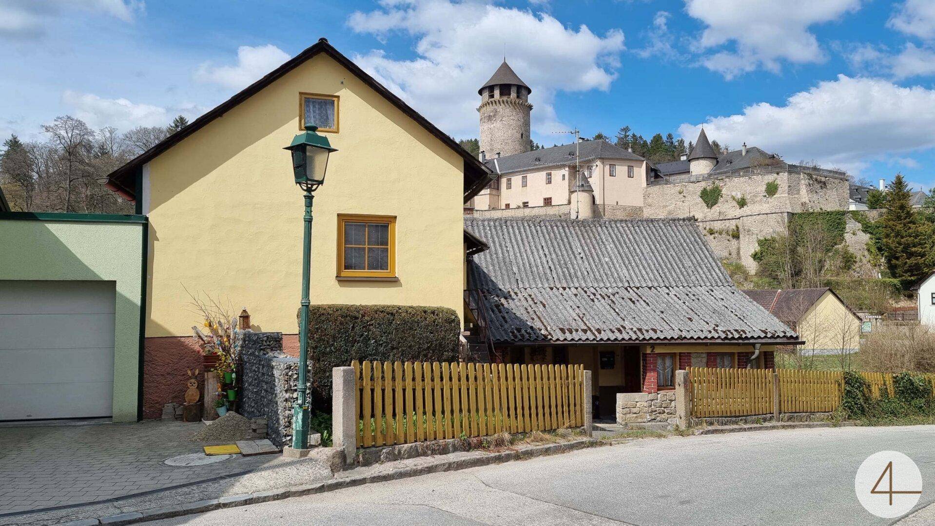 Gelbes Haus mit Blick auf eine historische Burg und ländliche Umgebung unter blauem Himmel.