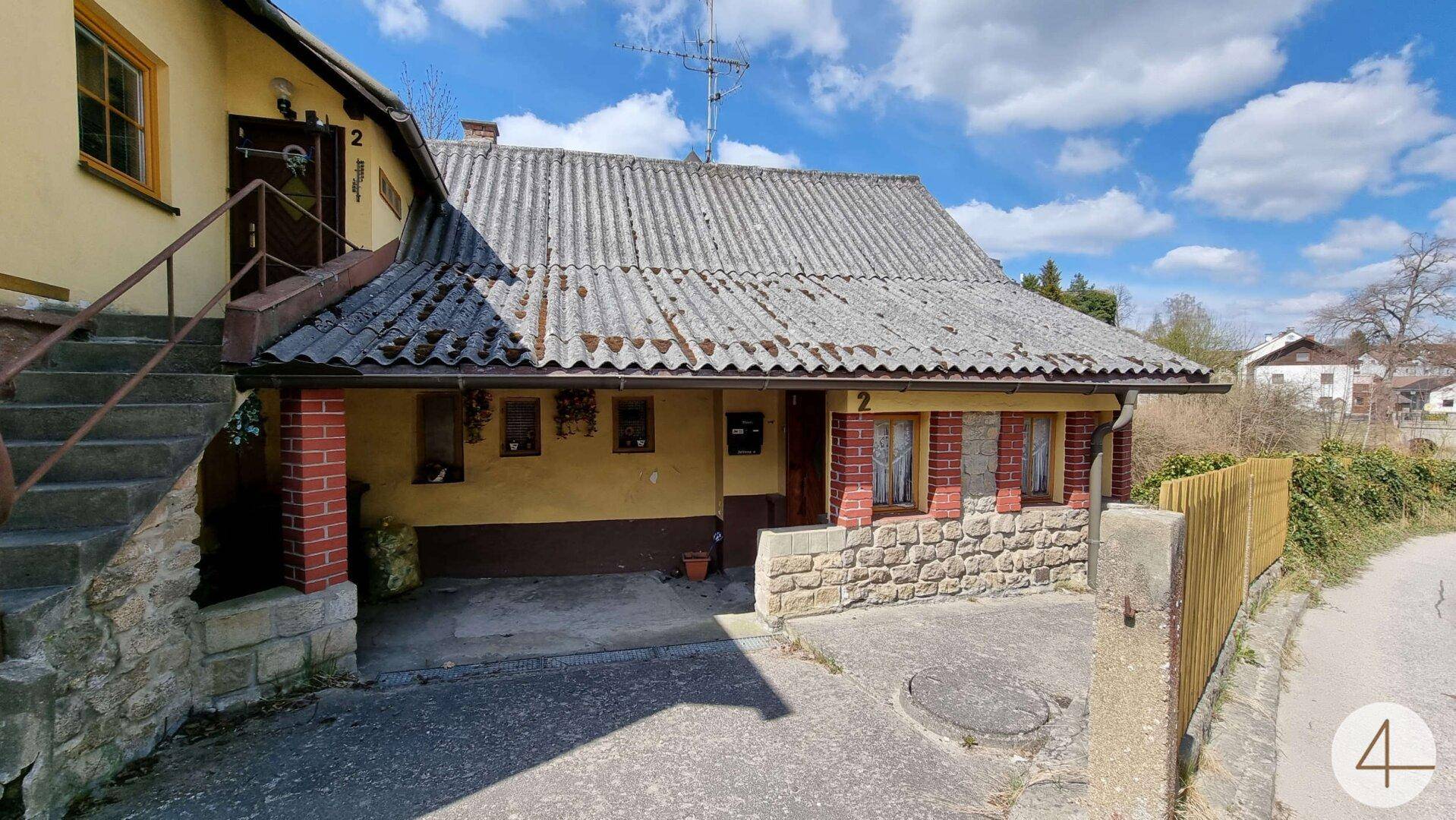 Vorderansicht eines älteren Hauses mit Steinfassade und überdachtem Eingangsbereich.