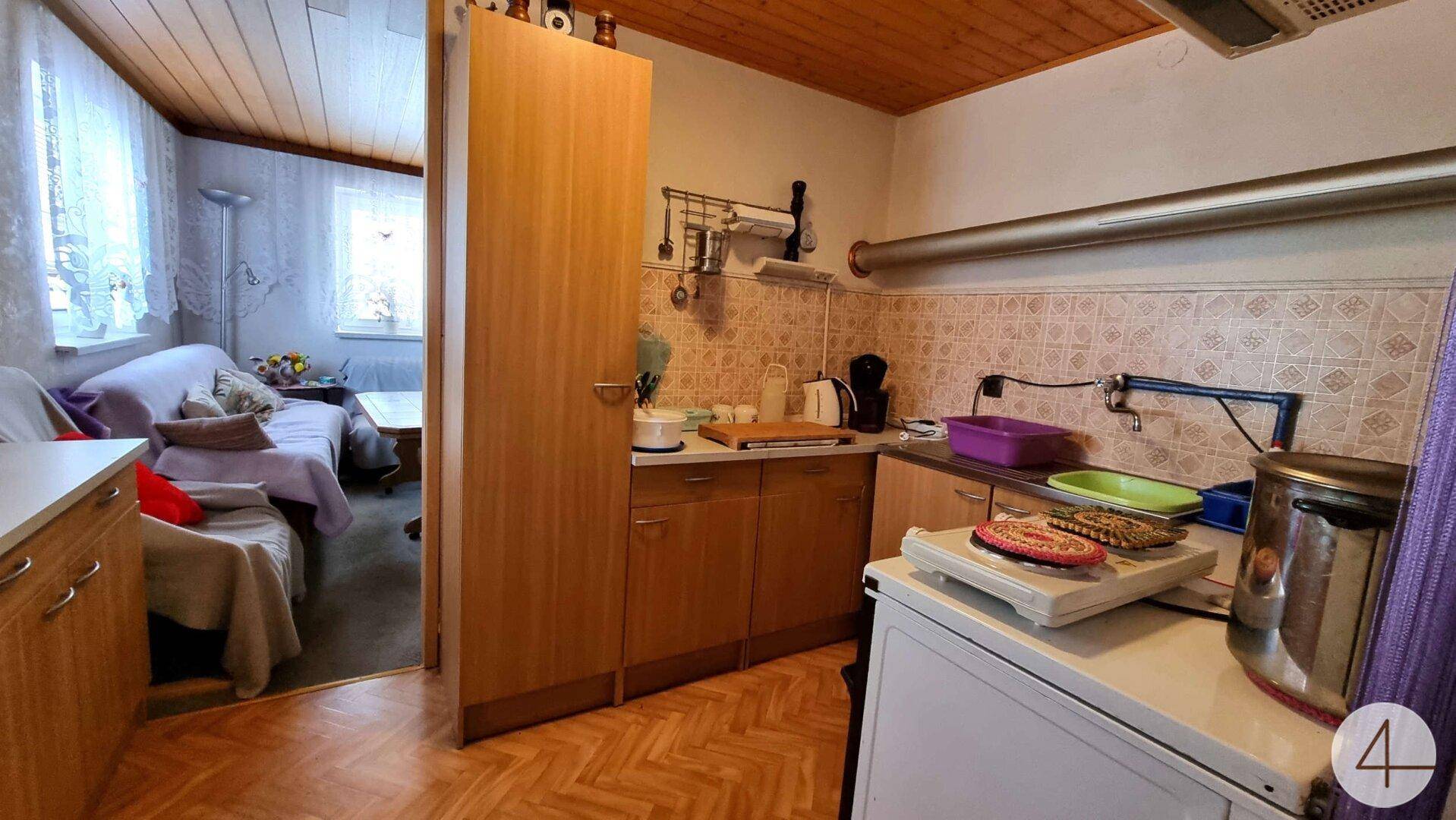 Kleine Küche mit Holzschränken, gefliestem Spritzschutz und Blick in den Wohnbereich.