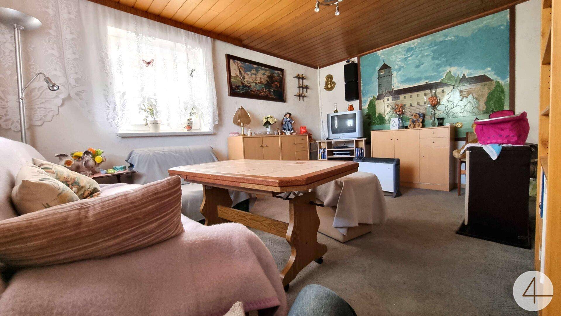 Gemütliches Wohnzimmer mit Teppichboden, Holzdecke und einem Wandgemälde einer Burg.