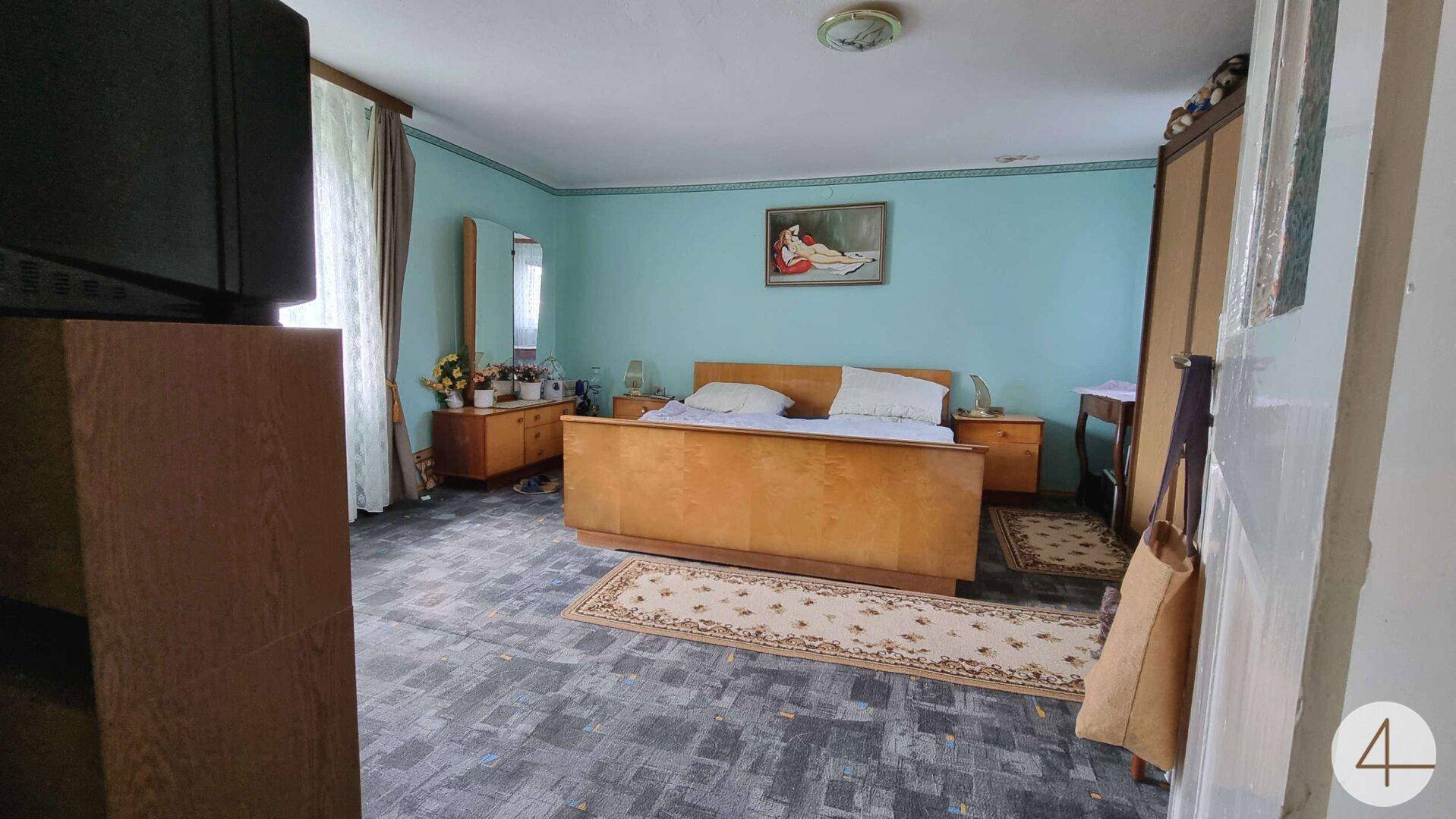 Schlafzimmer mit hellblauen Wänden, Holzmöbeln und einem Teppich auf dem Boden.