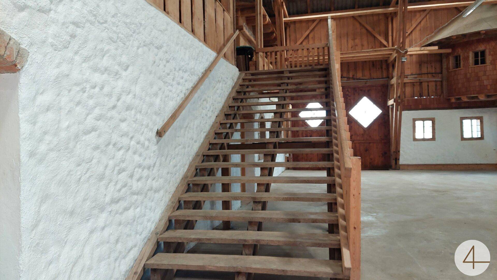 Rustikale Holztreppe mit weiß verputzter Wand in einem großen, offenen Innenraum.