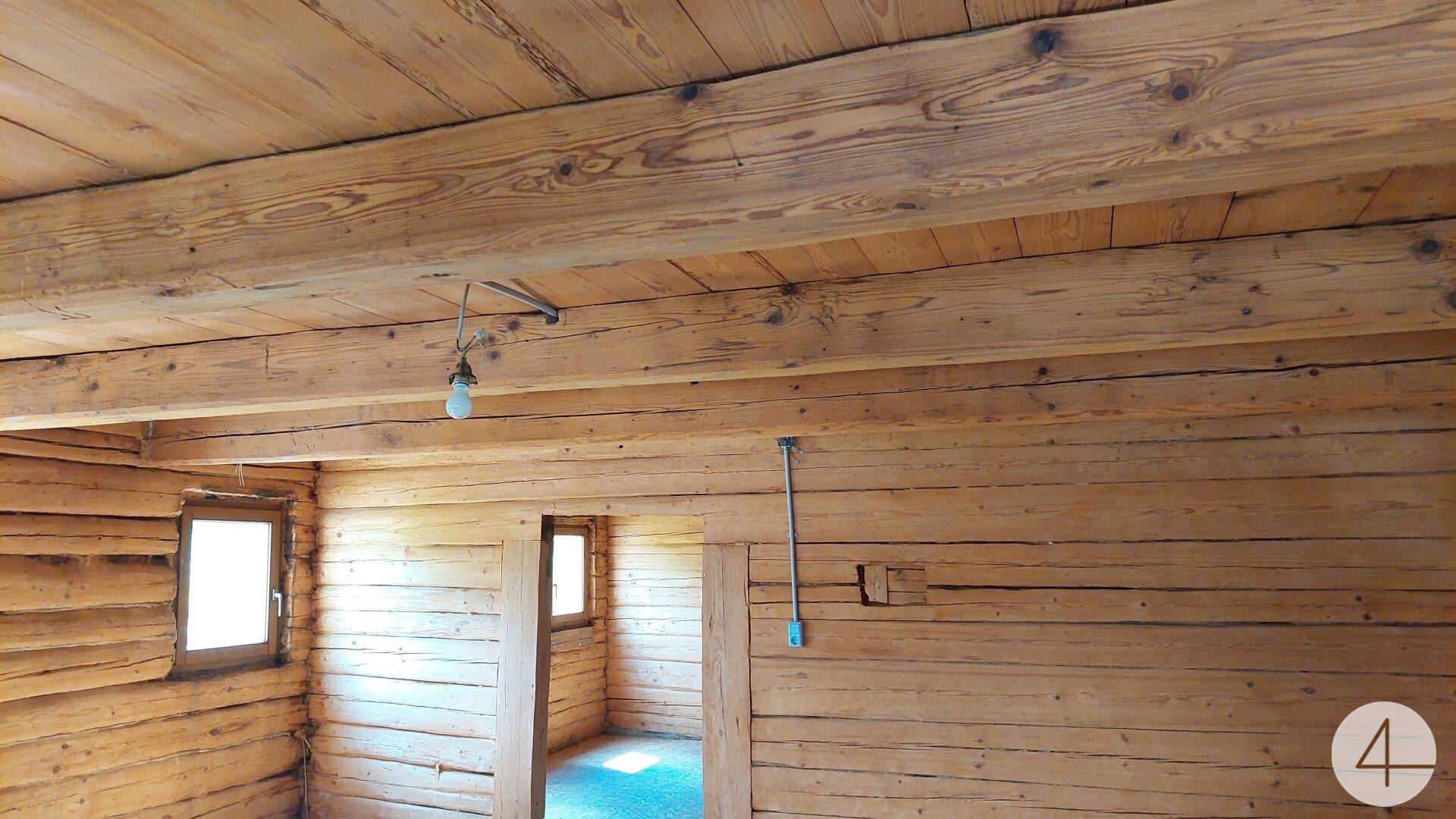 Innenraum mit Holzwänden und sichtbaren Holzbalken an der Decke, hell beleuchtet.