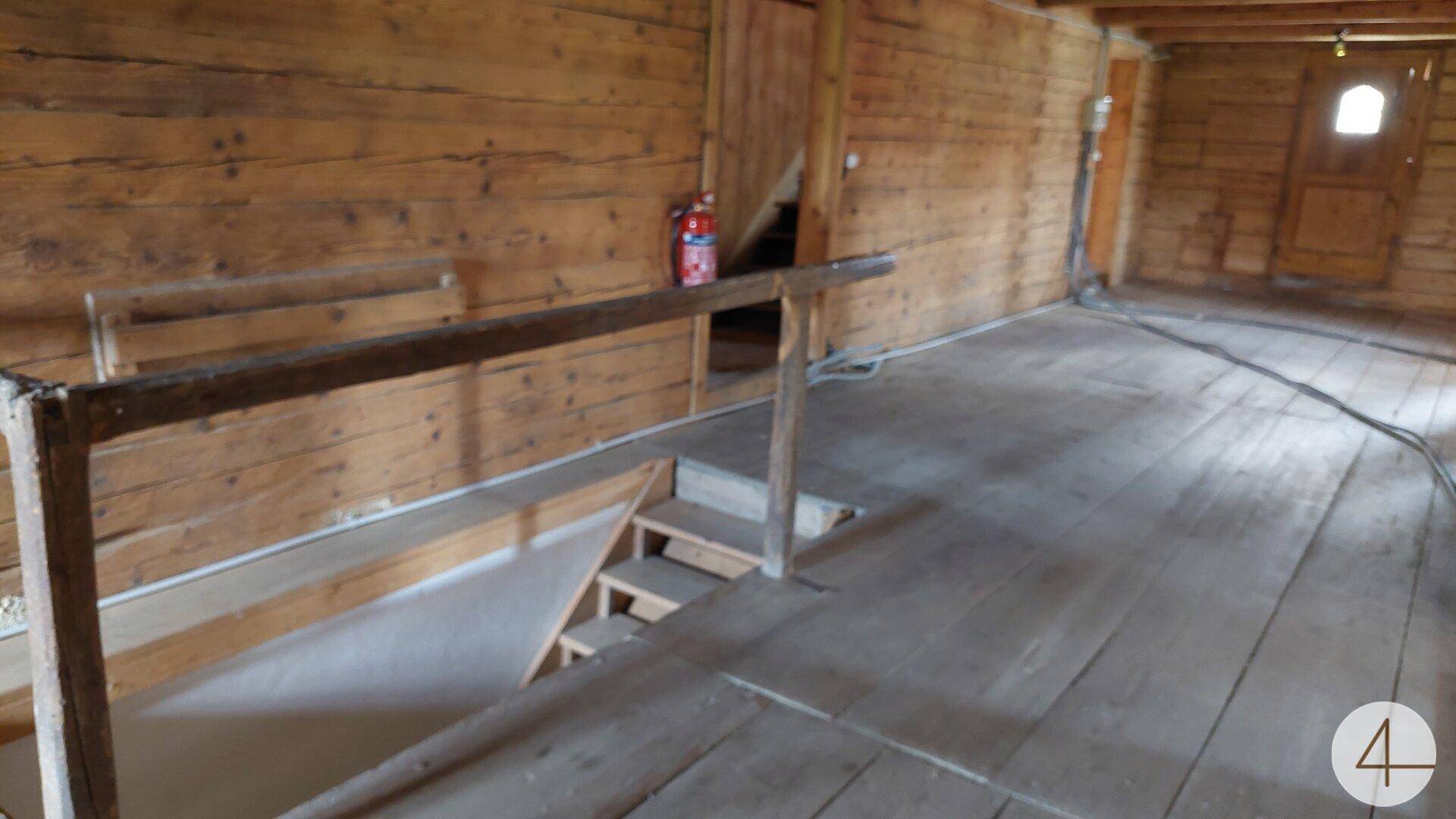 Raum mit Holzboden und einer Holztreppe, die in einen unteren Bereich führt.