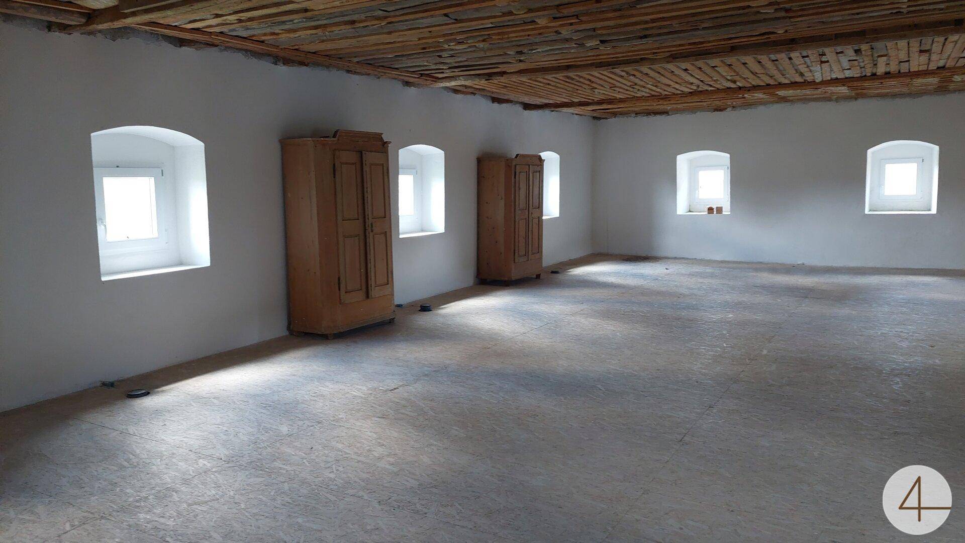 Heller Raum mit weißen Wänden, kleinen Fenstern und zwei Holzschränken.