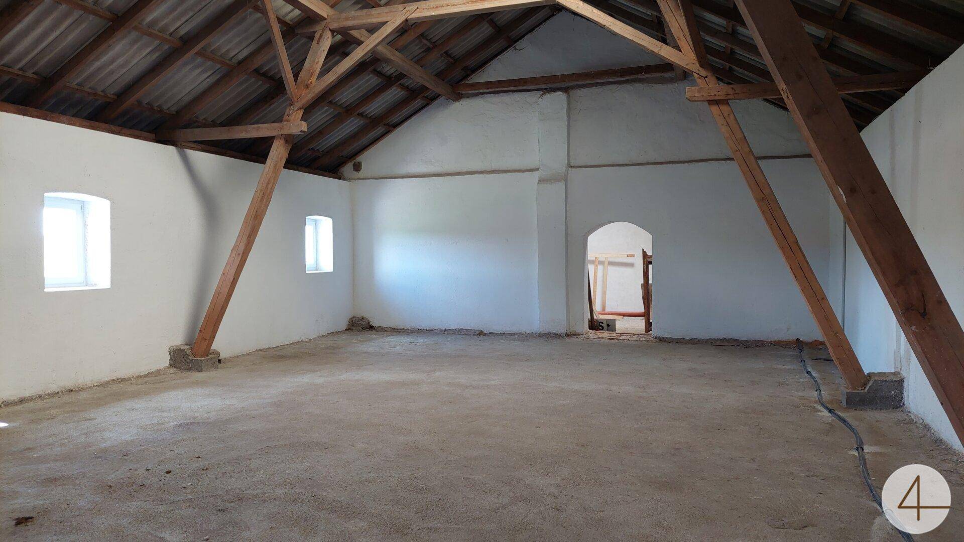 Geräumiger Dachboden mit sichtbaren Holzbalken und weiß verputzten Wänden, hell beleuchtet.