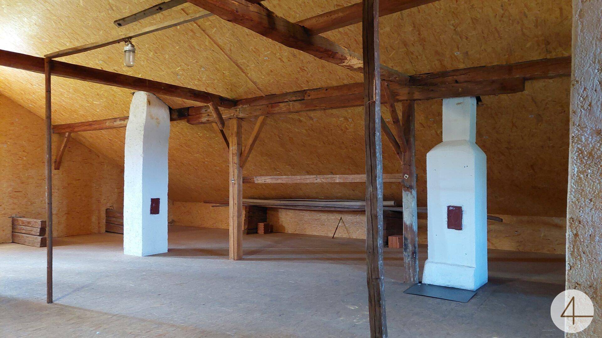 Großer Dachboden mit sichtbaren Holzbalken und zwei gemauerten Kaminen, bietet viel Platz.