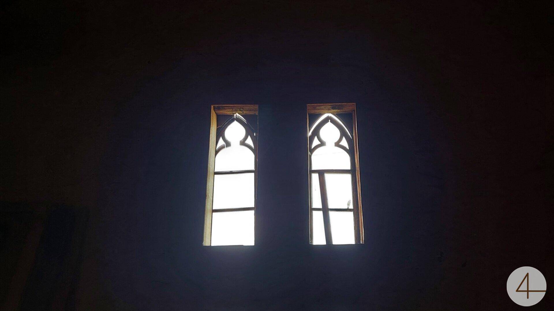 Zwei kleine, kunstvoll gestaltete Fenster in einem dunklen Raum, die Licht hereinlassen.