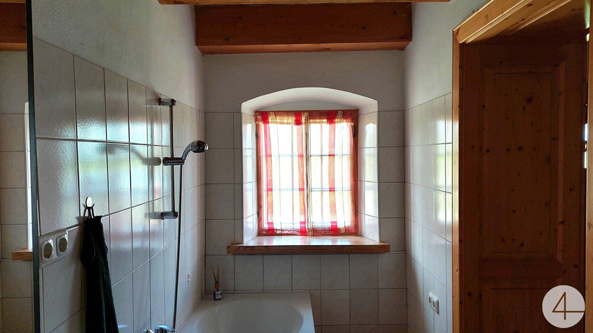 Badezimmer mit Fliesenwänden, einer Badewanne und einem Fenster mit rotem Vorhang.