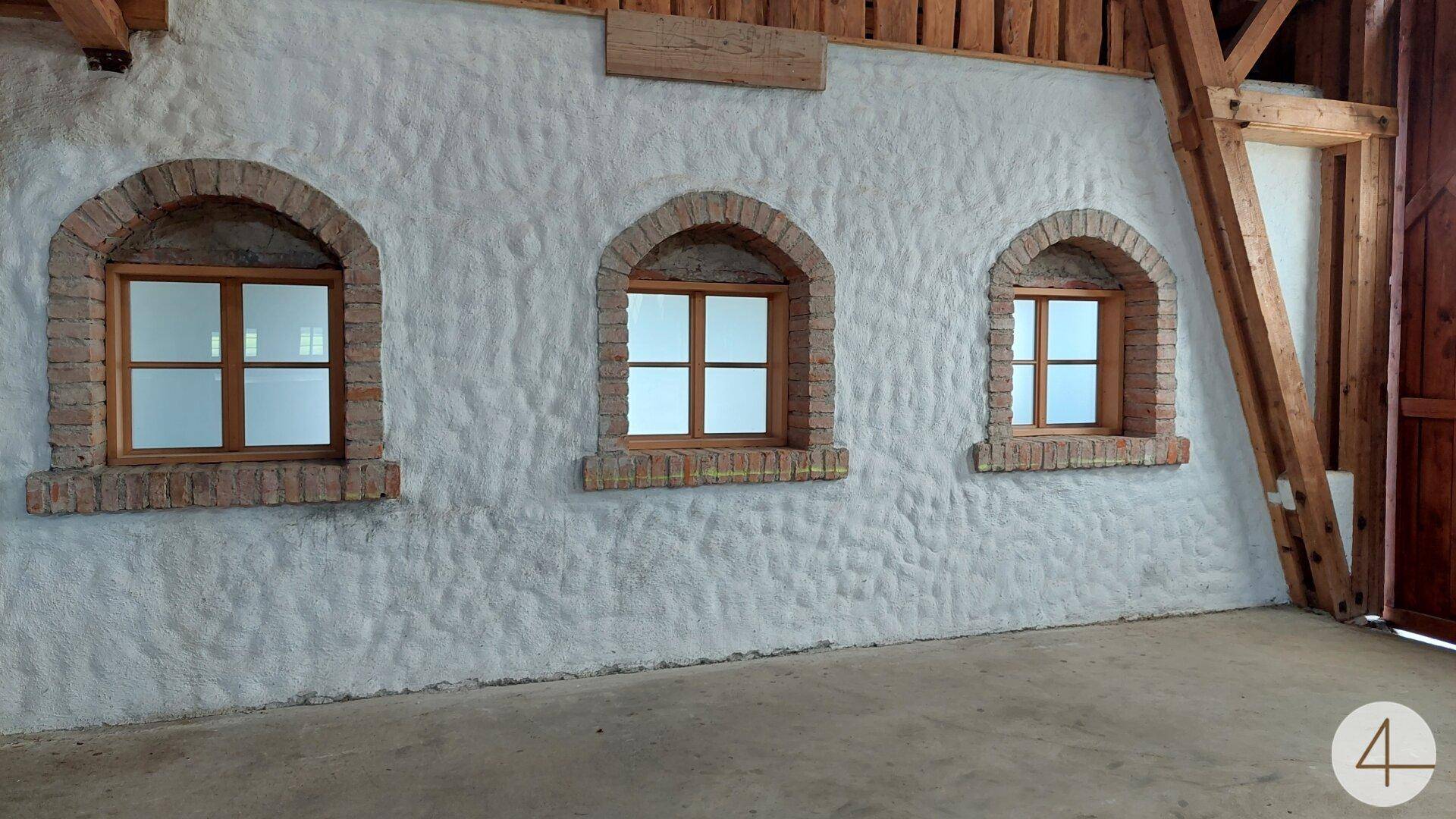 Innenwand mit drei Rundbogenfenstern und Ziegelumrandung, verputzt in rustikalem Stil.
