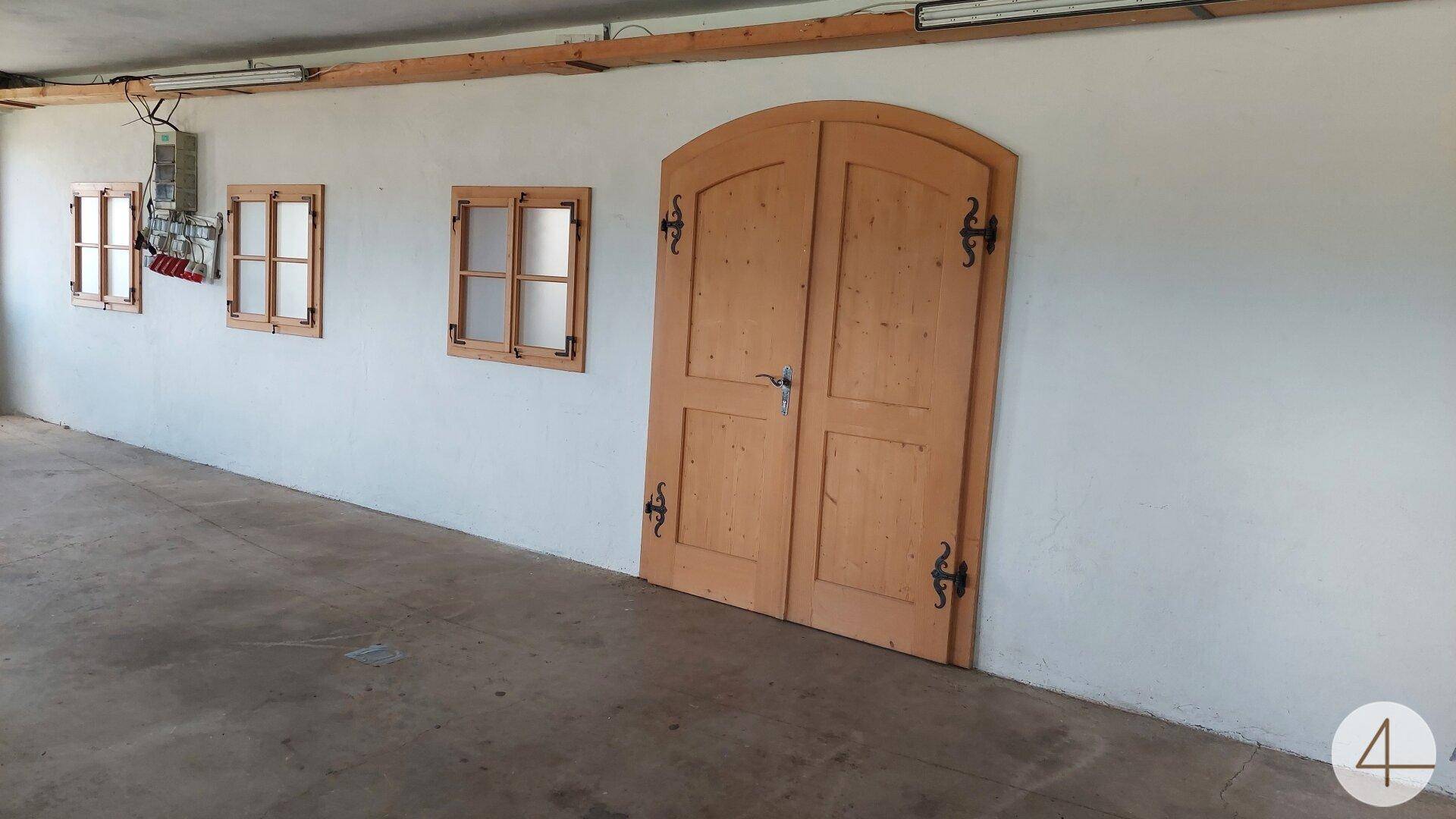 Innenraum mit weiß verputzten Wänden, kleinen Fenstern und einer großen Holztür im Landhausstil.