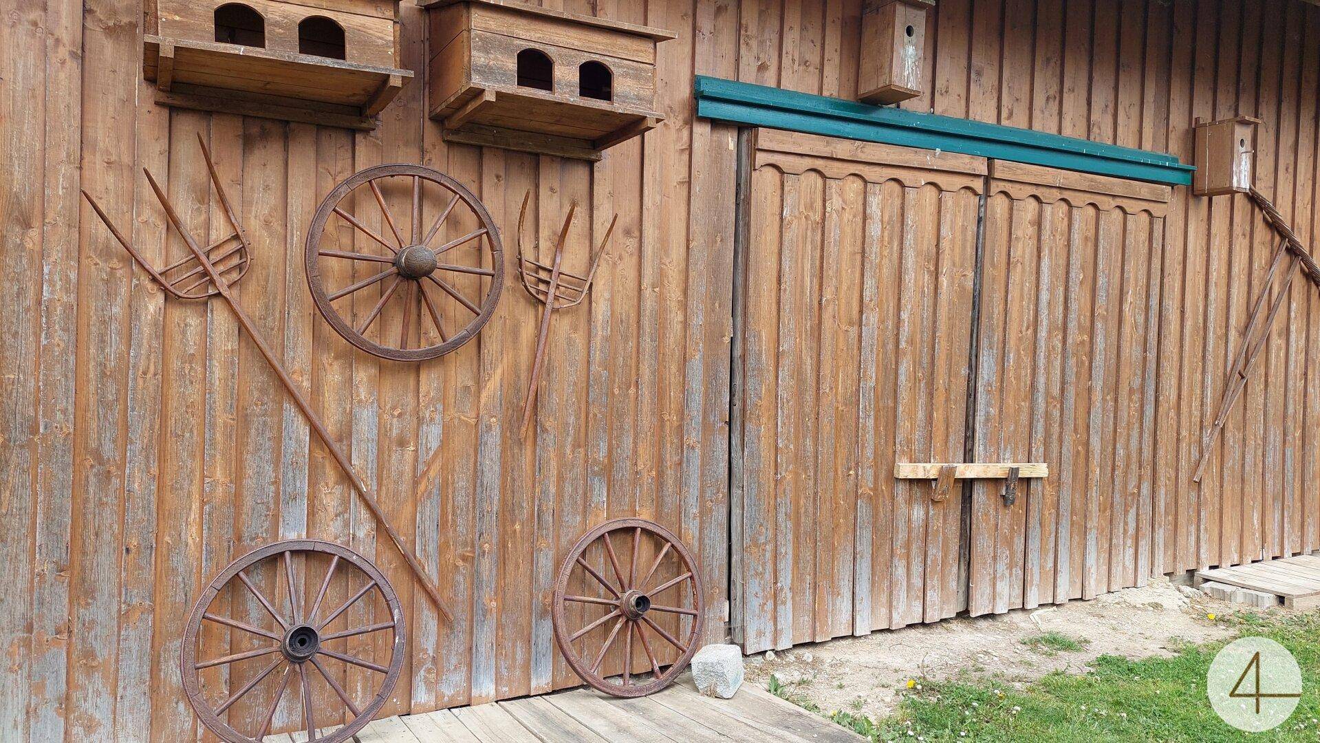 Detailansicht der Holzfassade eines rustikalen Gebäudes mit alten Wagenrädern und Vogelhäusern.