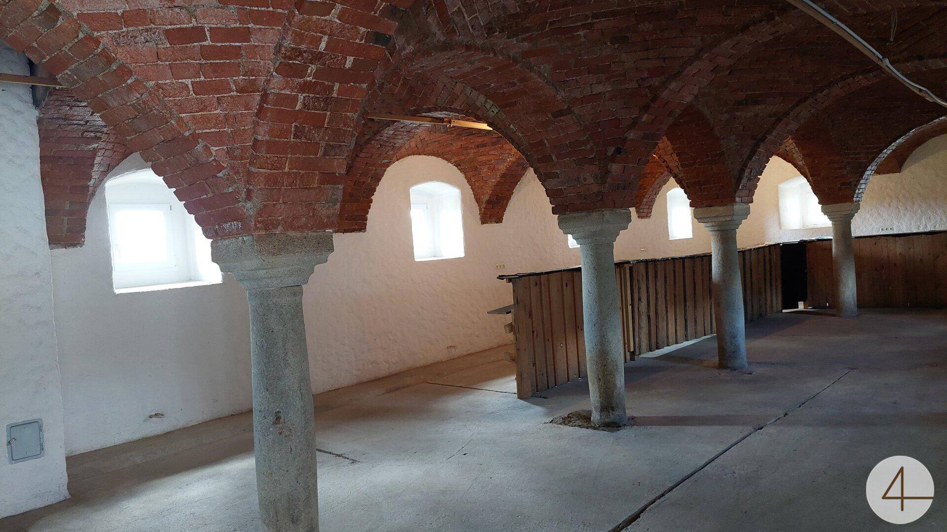 Historischer Gewölbekeller mit Ziegelbögen, Steinsäulen und kleinen Fenstern, hell beleuchtet.