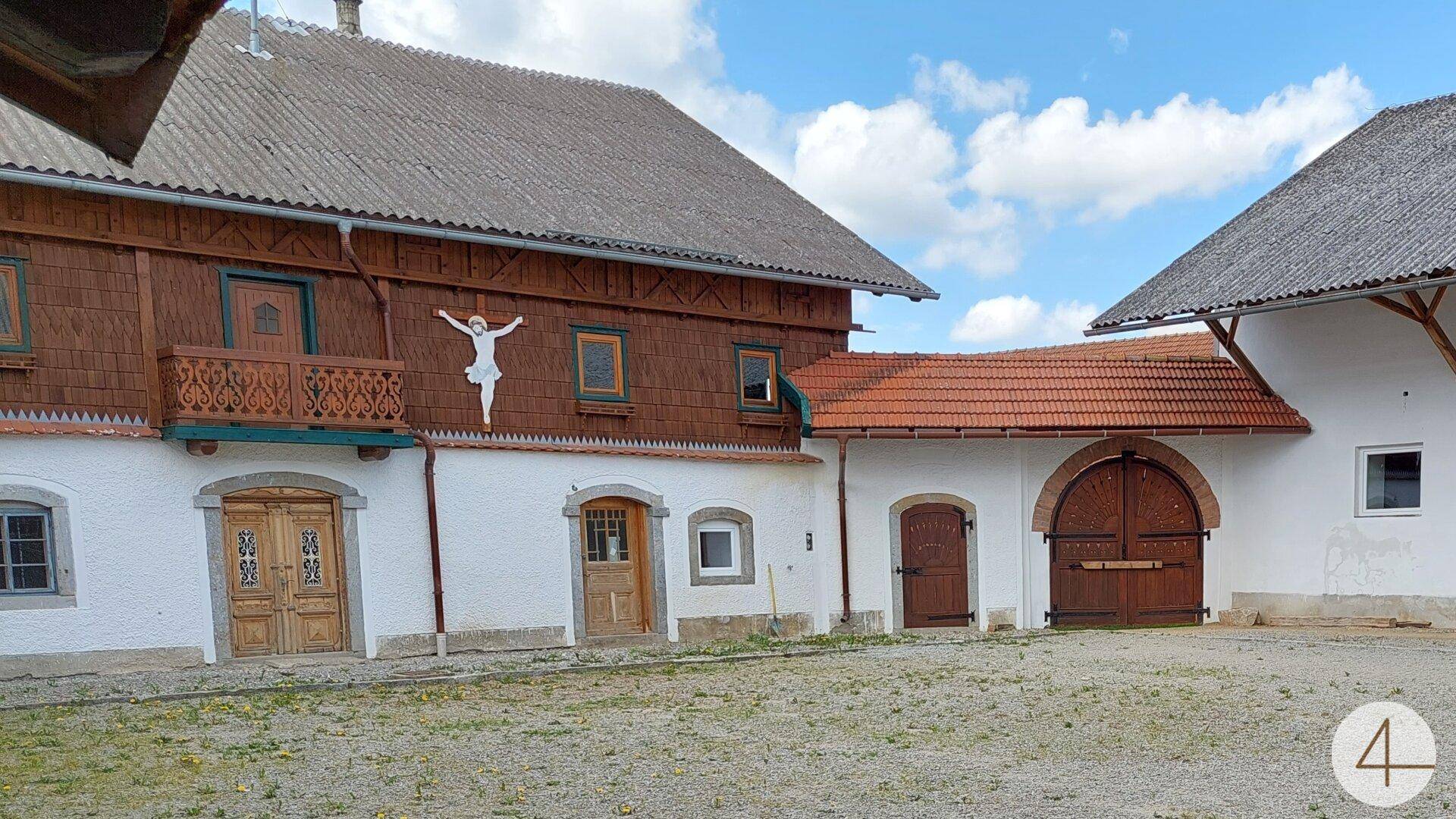 Traditionelles Bauernhausensemble mit Holzbalkon und weißer Fassade, umgeben von einem Kieshof.