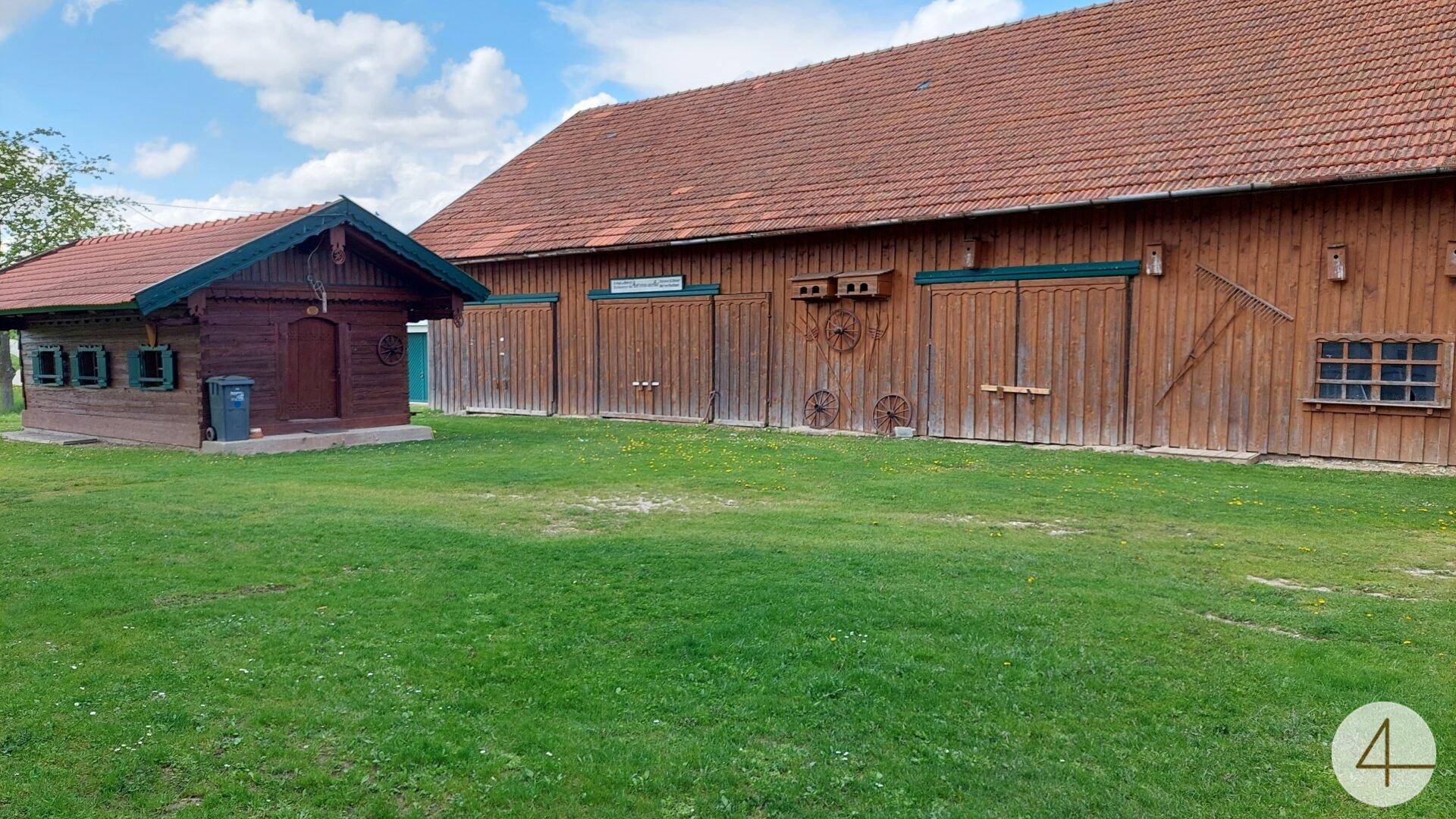 Weitläufige grüne Wiese mit einem großen Holzgebäude und einem kleinen Holzhaus.
