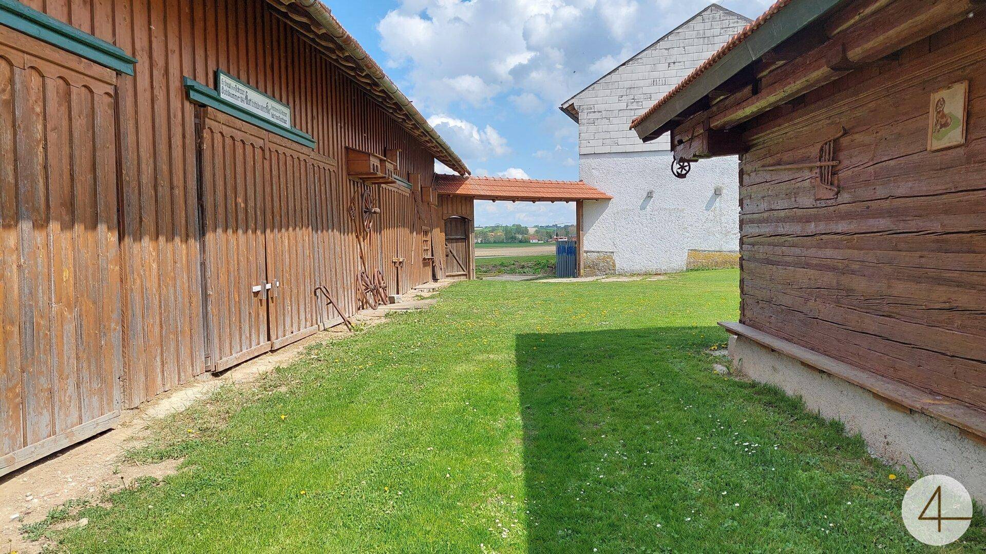 Grüner Weg zwischen zwei traditionellen Holzgebäuden, führt in die offene Landschaft.