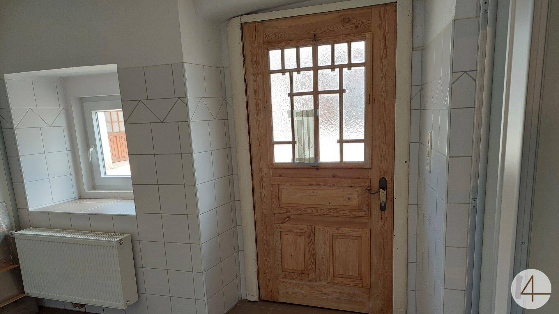 Badezimmer mit weißen Fliesen, einem Fenster und einer Holztür mit Glaseinsätzen.