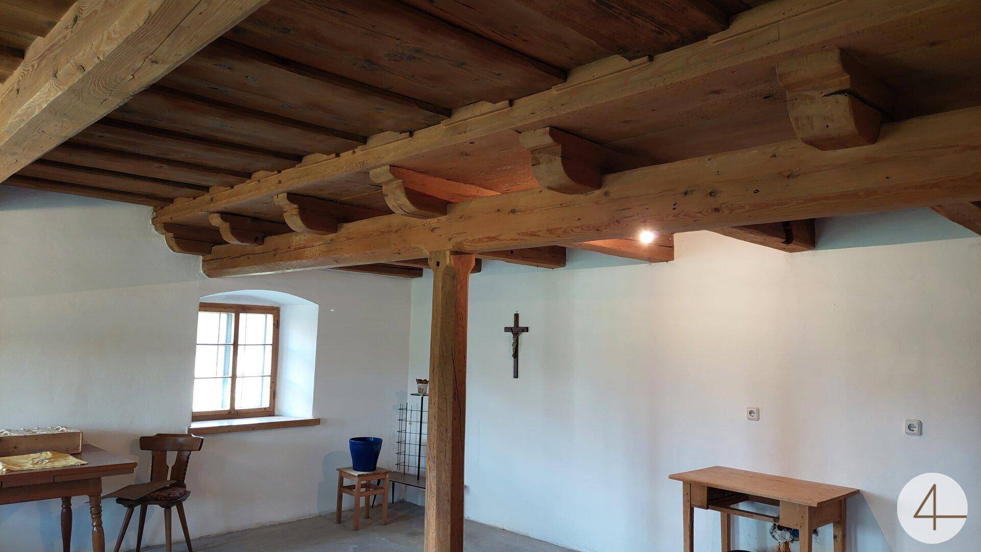 Gemütlicher Raum mit Holzbalkendecke, weiß verputzten Wänden und einem Fenster, traditionell eingerichtet.