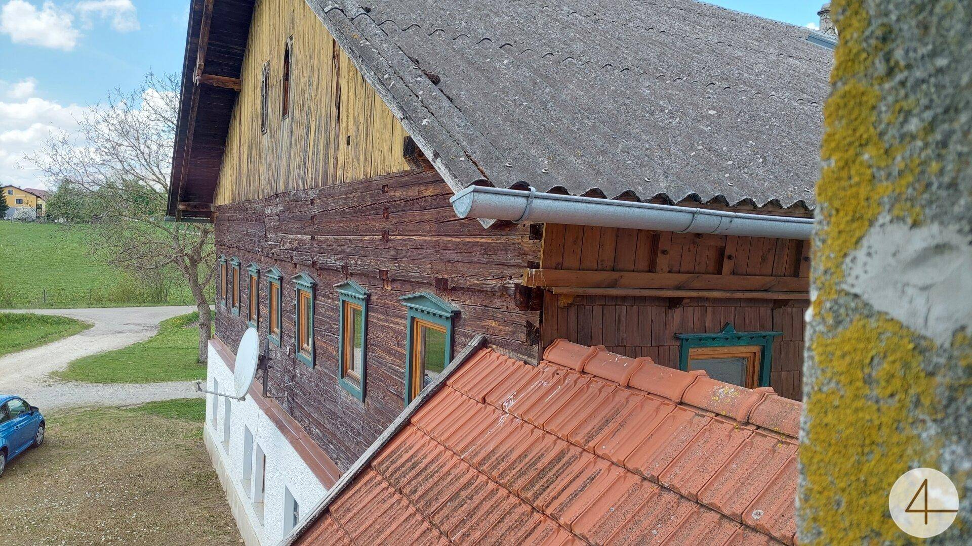 Blick auf ein traditionelles Ziegeldach und die Holzfassade eines alten Bauernhauses.