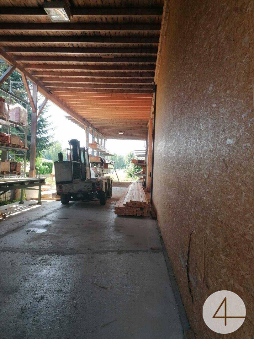 Überdachter Außenbereich einer Werkstatt mit Holzdecke, Betonboden und einem Gabelstapler.