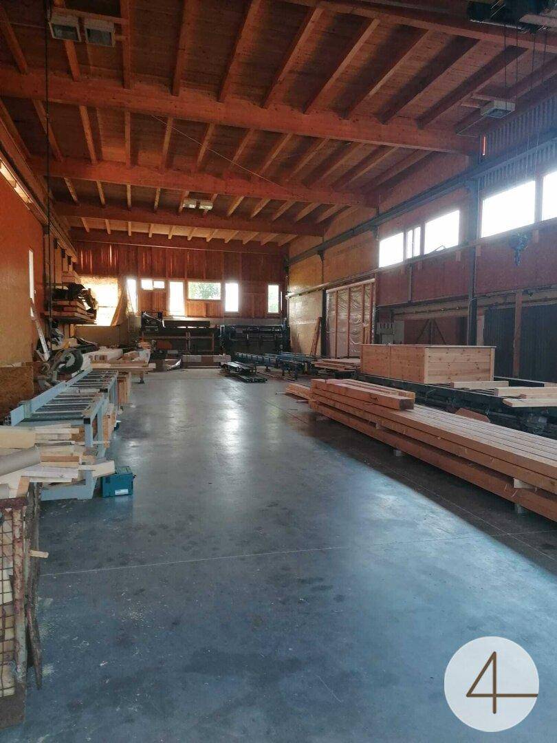 Große Werkshalle mit Holzbalkendecke, Betonboden und gestapelten Holzmaterialien.
