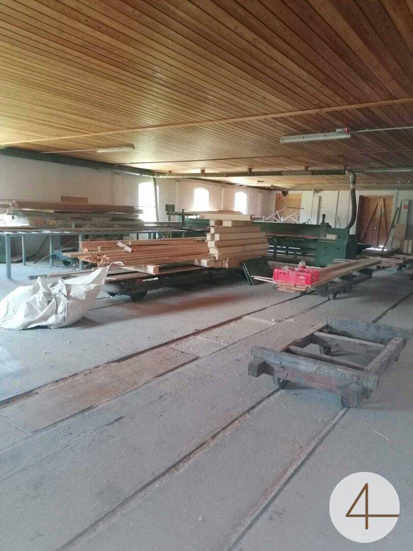 Werkstattraum mit Holzdecke, Betonboden und verschiedenen Holzbearbeitungsmaschinen und Materialien.